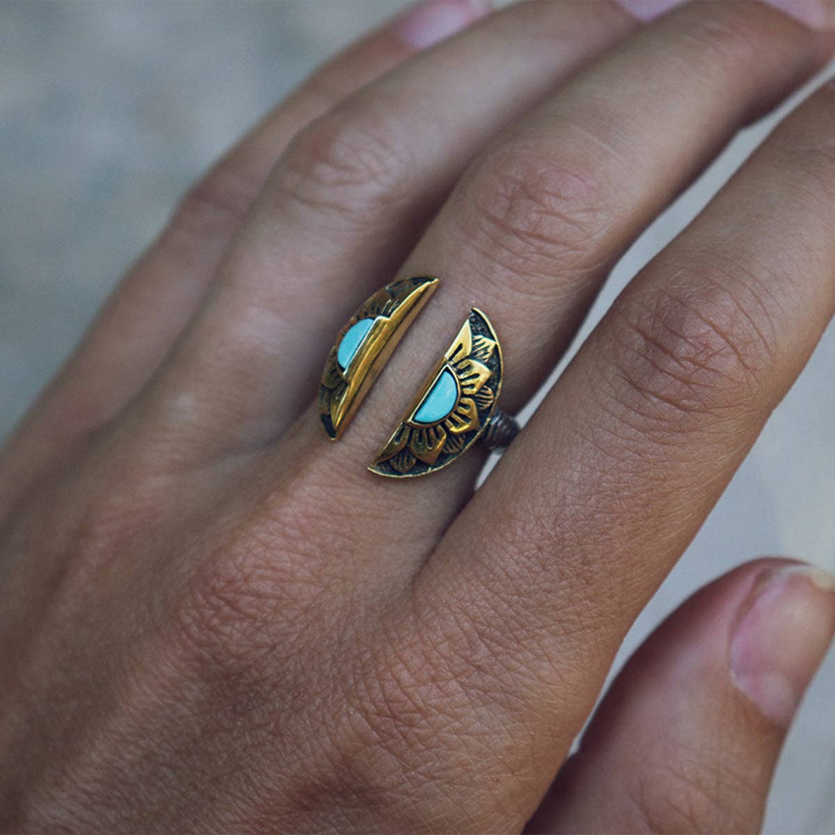 A hand wears the bahgsu jewels Natural Mystic Ring - Turquoise, an adjustable piece featuring gold and turquoise accents in a two-part sunburst design flanking the finger.