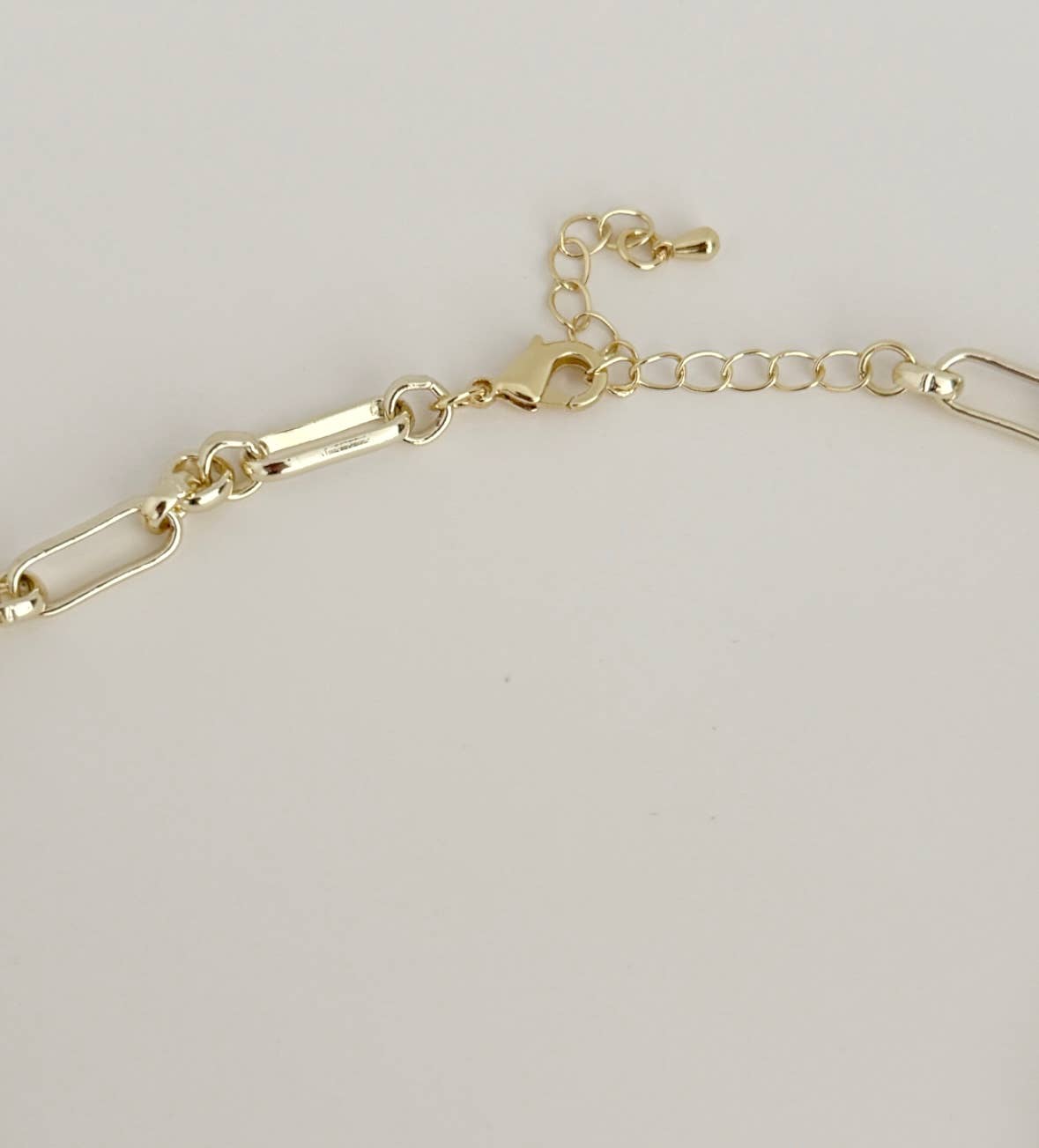 The Azure Tide Necklace by Tramps+Thieves features elongated gold links, an adjustable clasp, and a delicate blue stone charm, shown on a plain white background.
