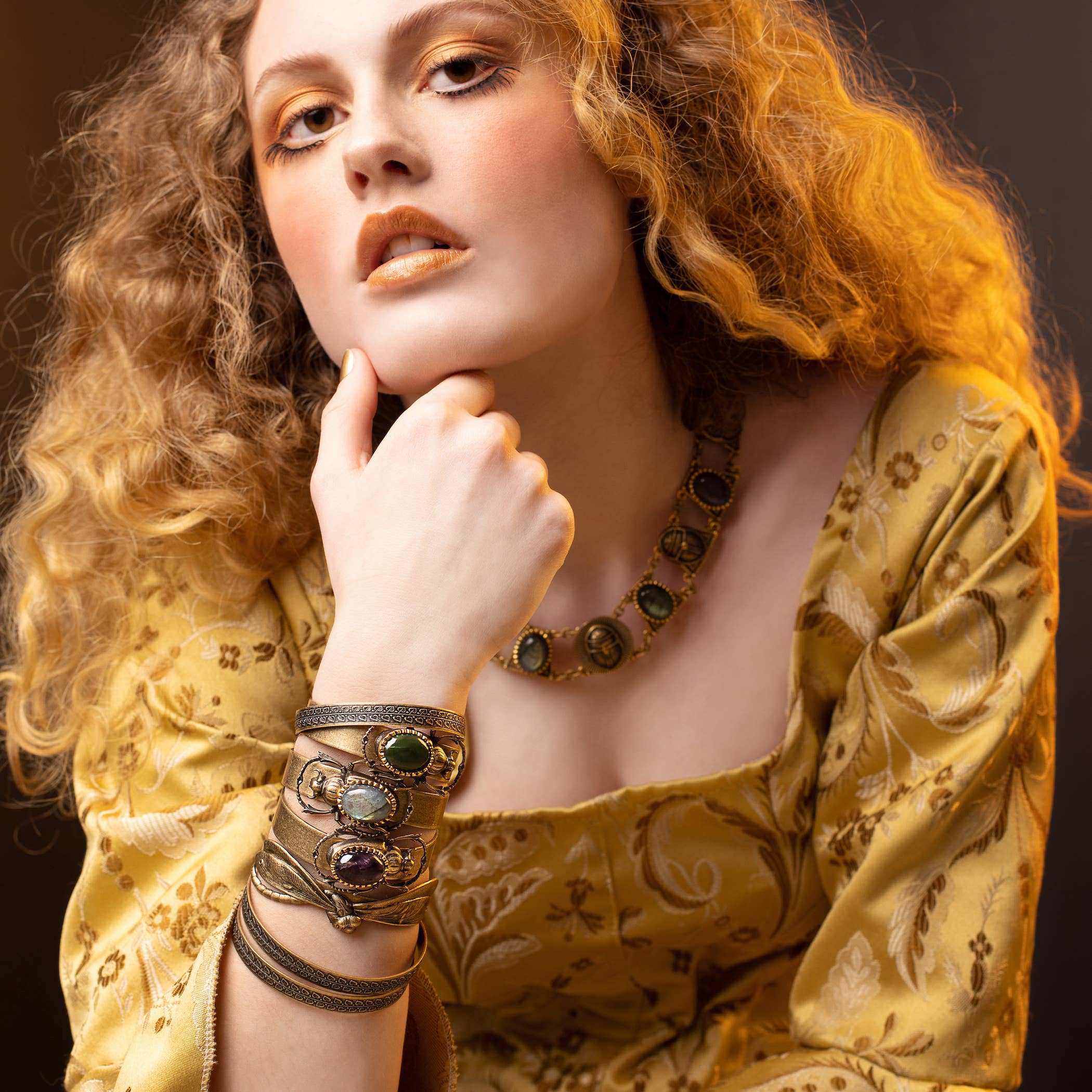 Close-up of a woman wearing a Sacred Scarab Cuff with gemstone details and golden-toned attire and makeup