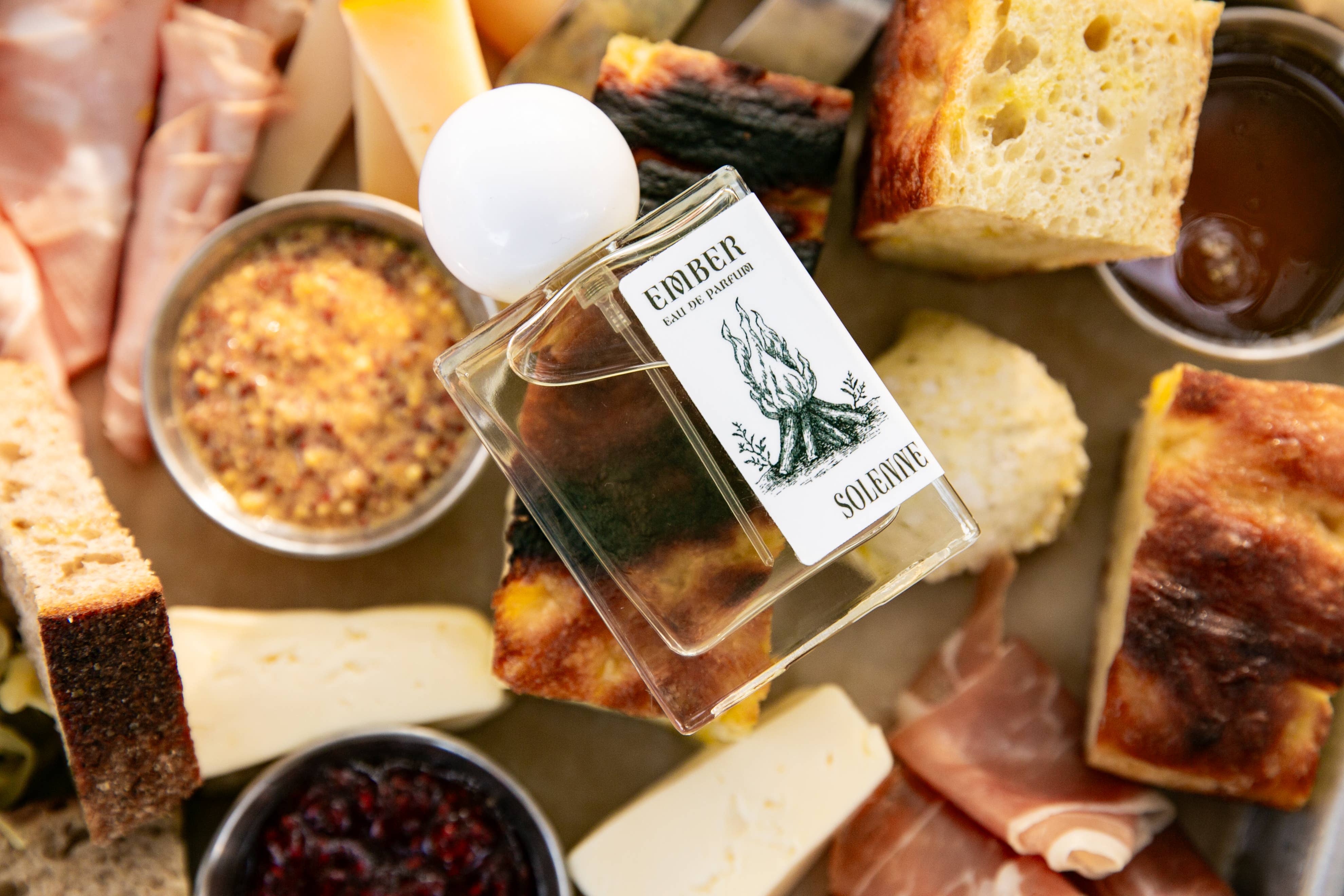 EMBER - Eau De Parfum - Nontoxic Fragrance bottle placed among artisan breads, cheeses, and spreads on a wooden board