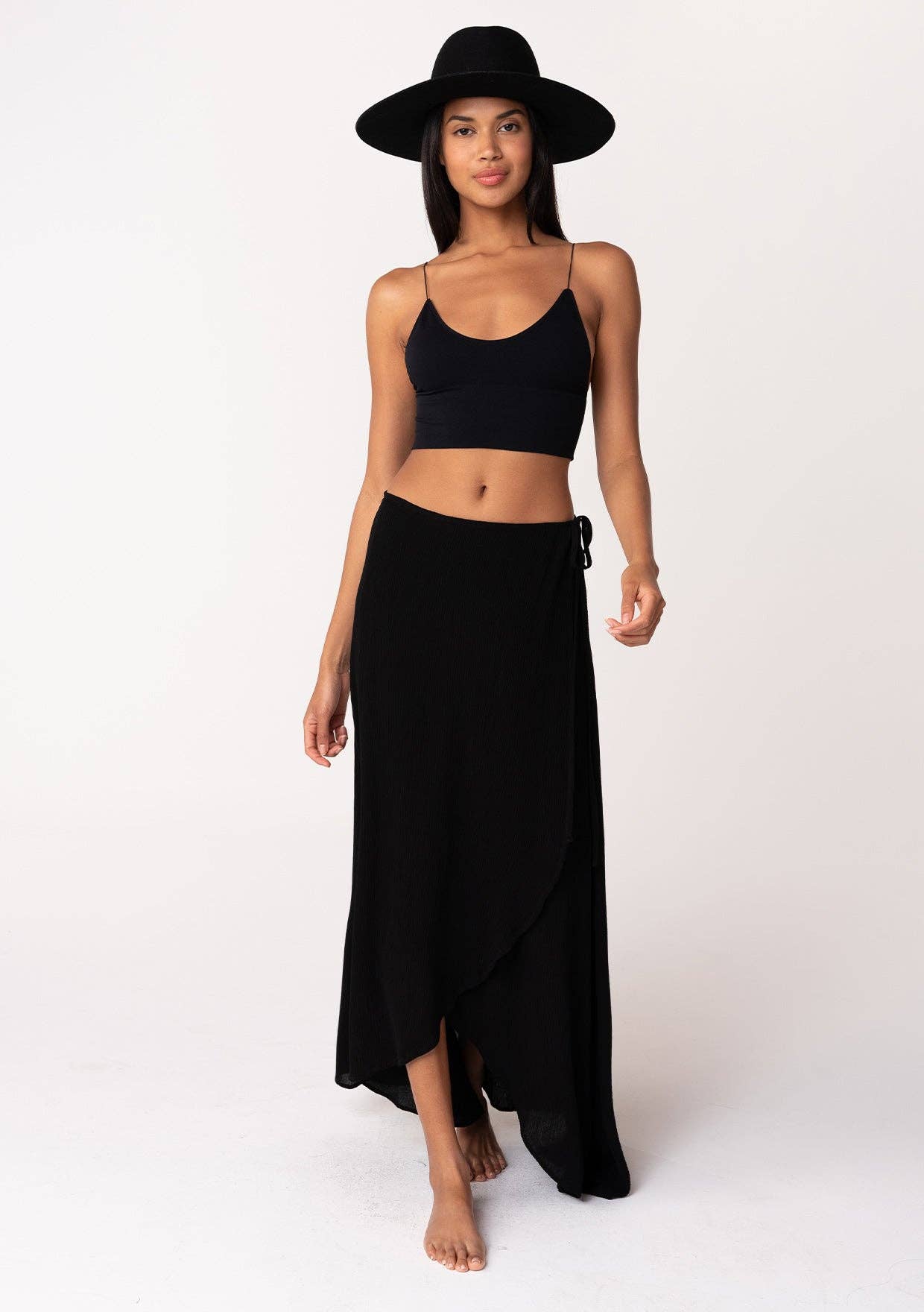 Woman wearing a black Summer Solid Wrap Maxi Skirt paired with a black crop top and wide-brimmed hat.
