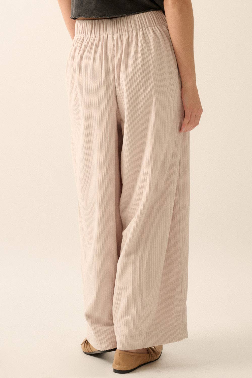 A person wears Promesa USA Velvet Corduroy Pleat-Front Wide-Leg Pants in light beige and tan flat shoes, standing with one arm by their side against a neutral background.