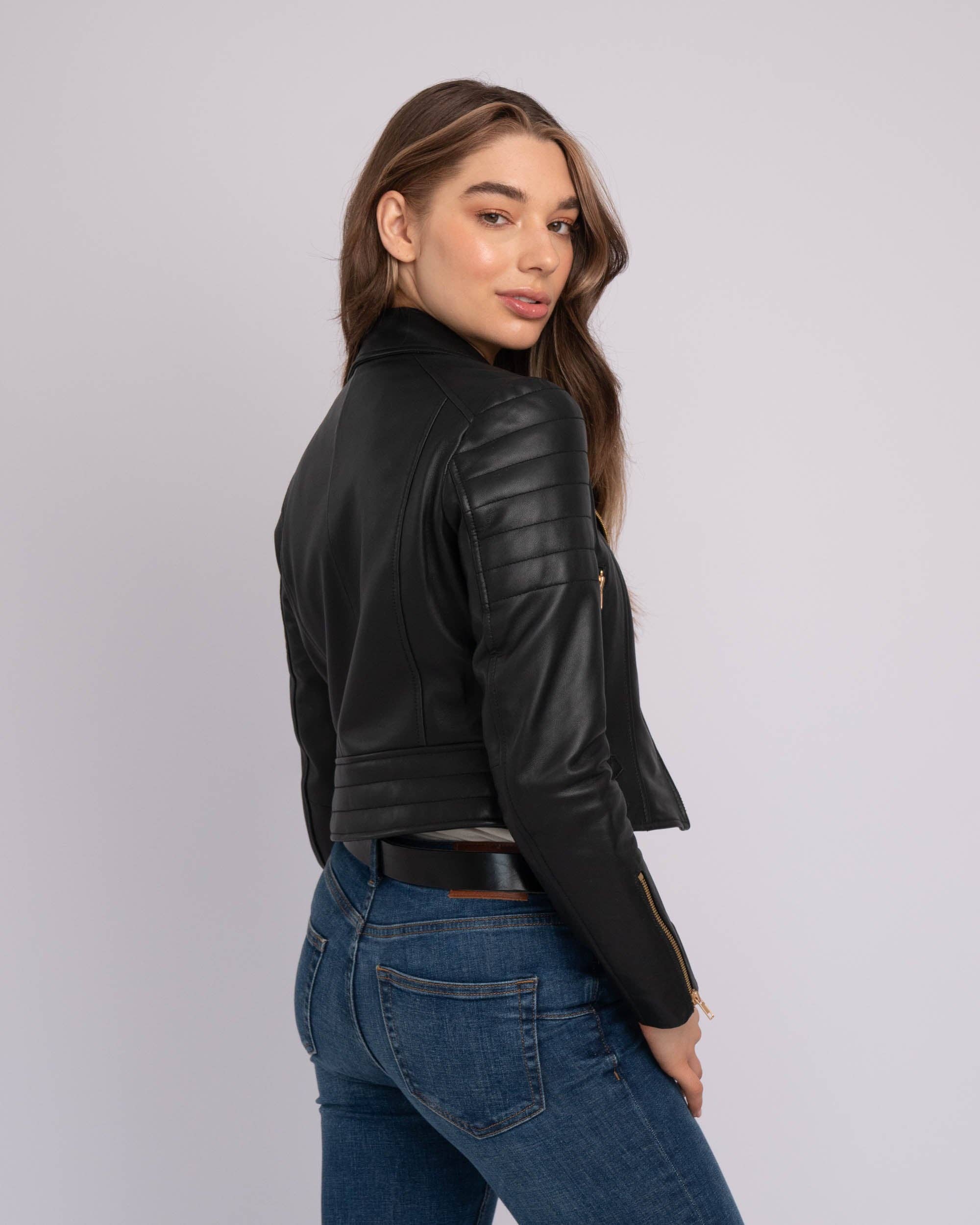 Woman wearing a black Eureka | Leather Biker Jacket with quilted detailing, paired with blue jeans against a plain backdrop.