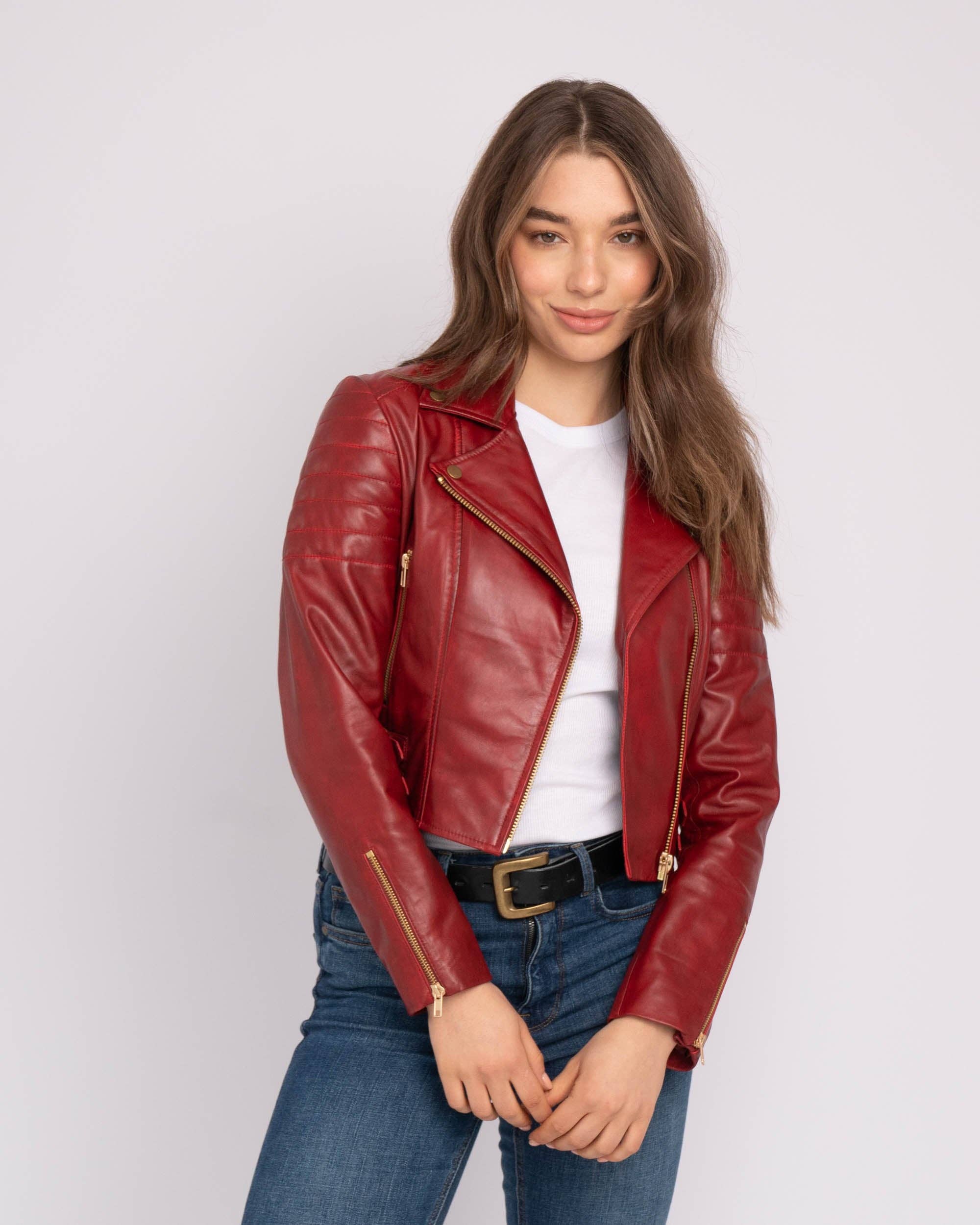 Woman wearing a red Eureka | Leather Biker Jacket with gold zippers, paired with a white top and blue jeans.