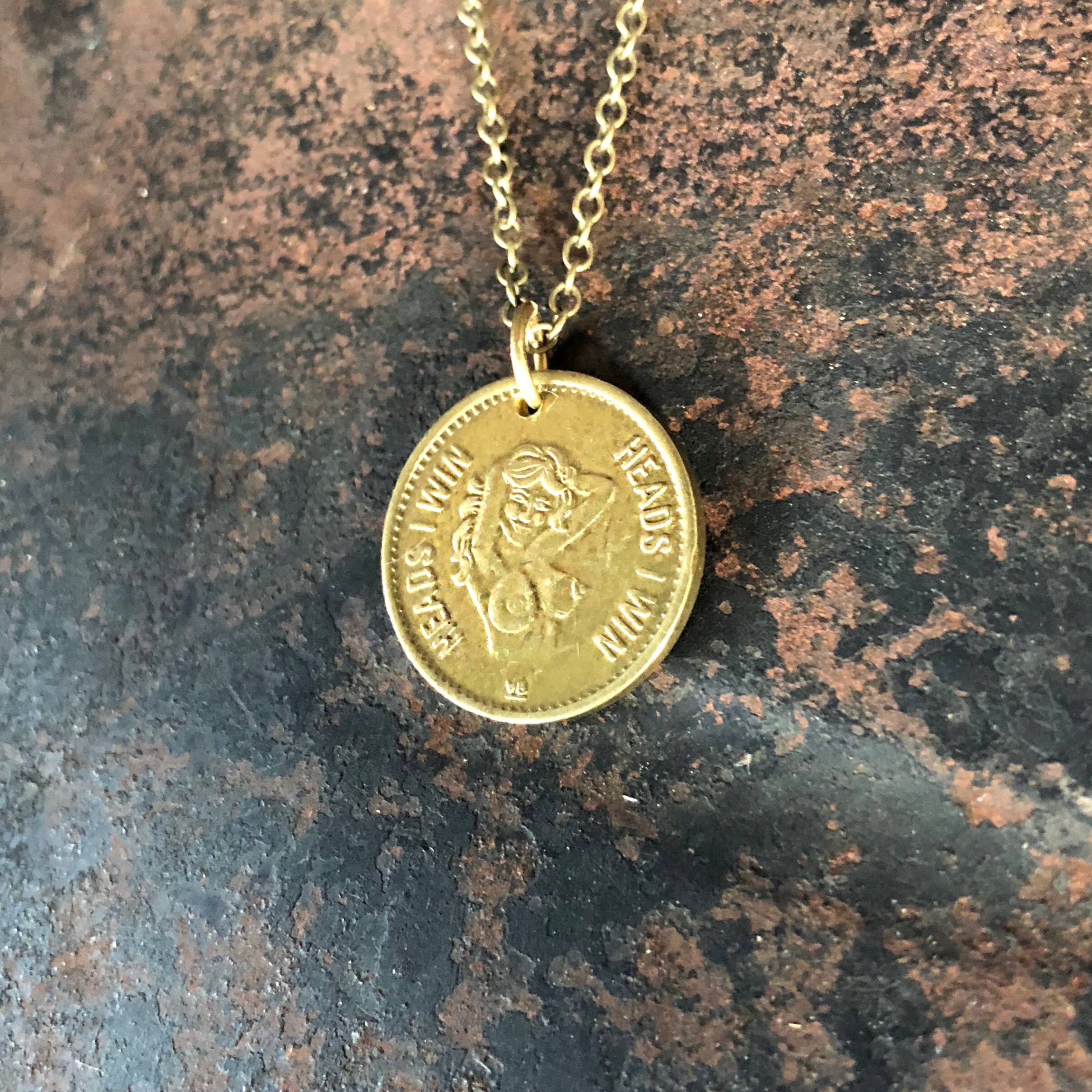 The Vintage Heads & Tails Peepshow Token Necklace by ASTALI features a coin pendant with embossed details on an antique brass chain, blending elegance and vintage flair for a standout collectible accessory.