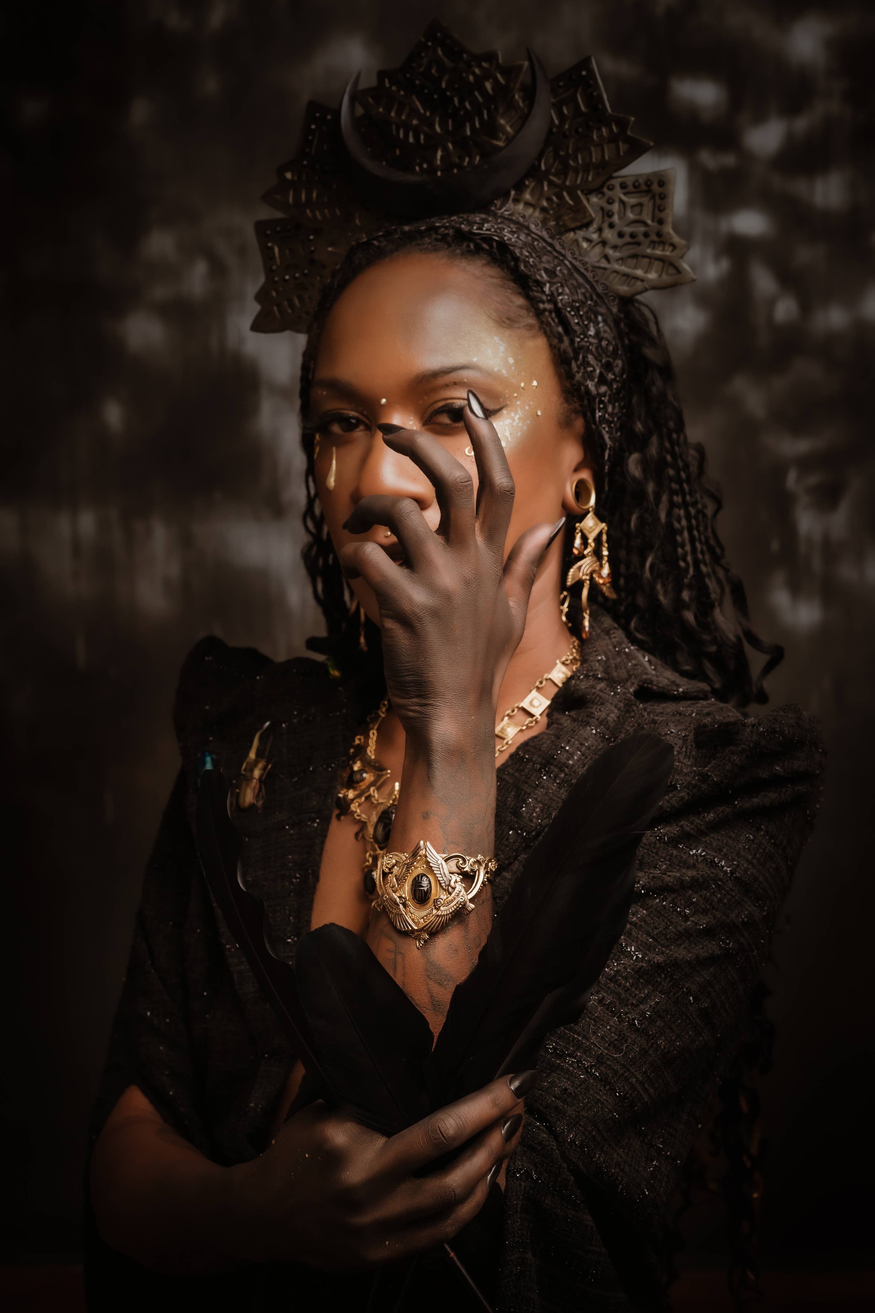 Woman in dark attire wearing gold earrings and a striking gold Nekhbet Shield Cuff bracelet with intricate details.