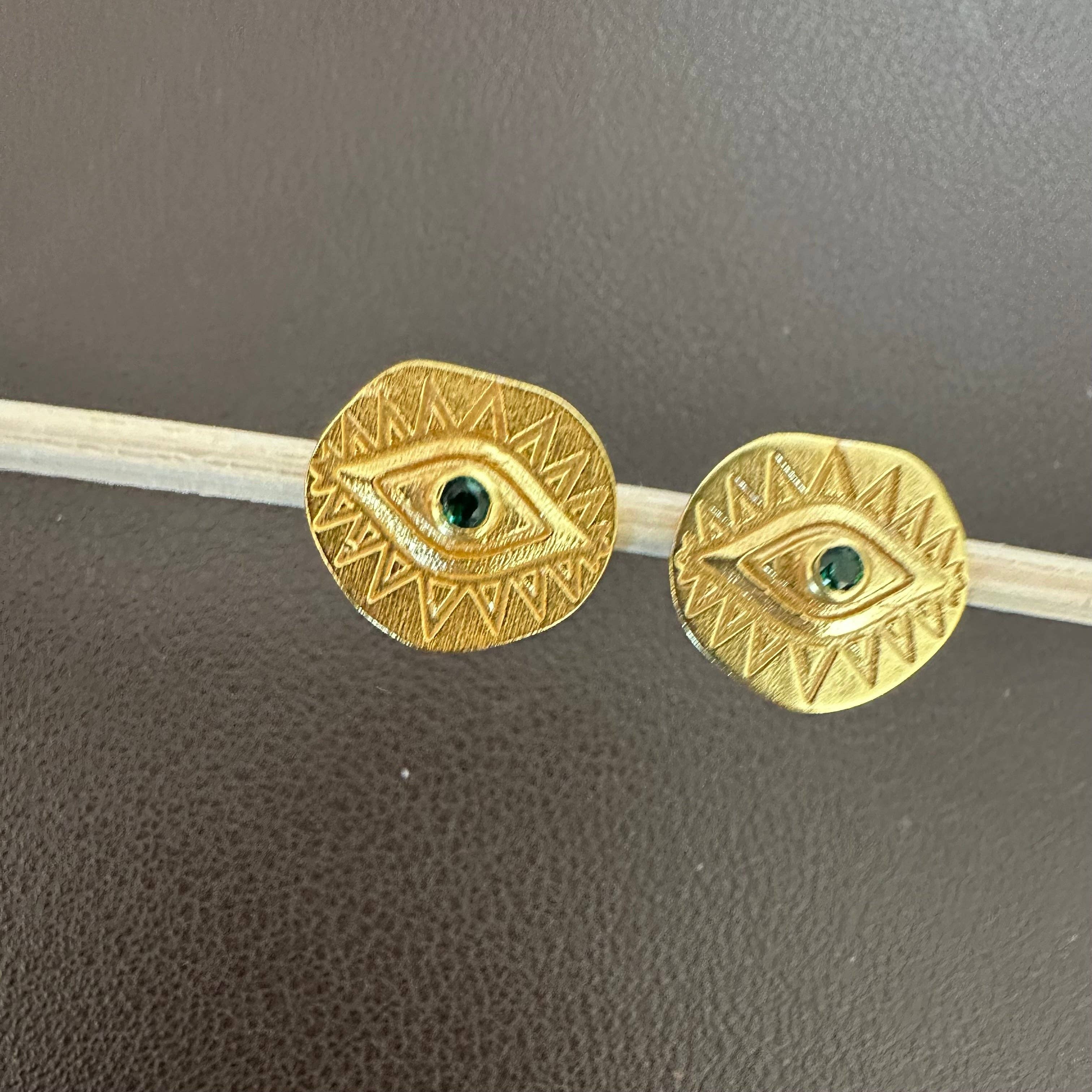 Third Eye | Evil Eye Earrings gold tone with green center stones and etched geometric designs on a brown background