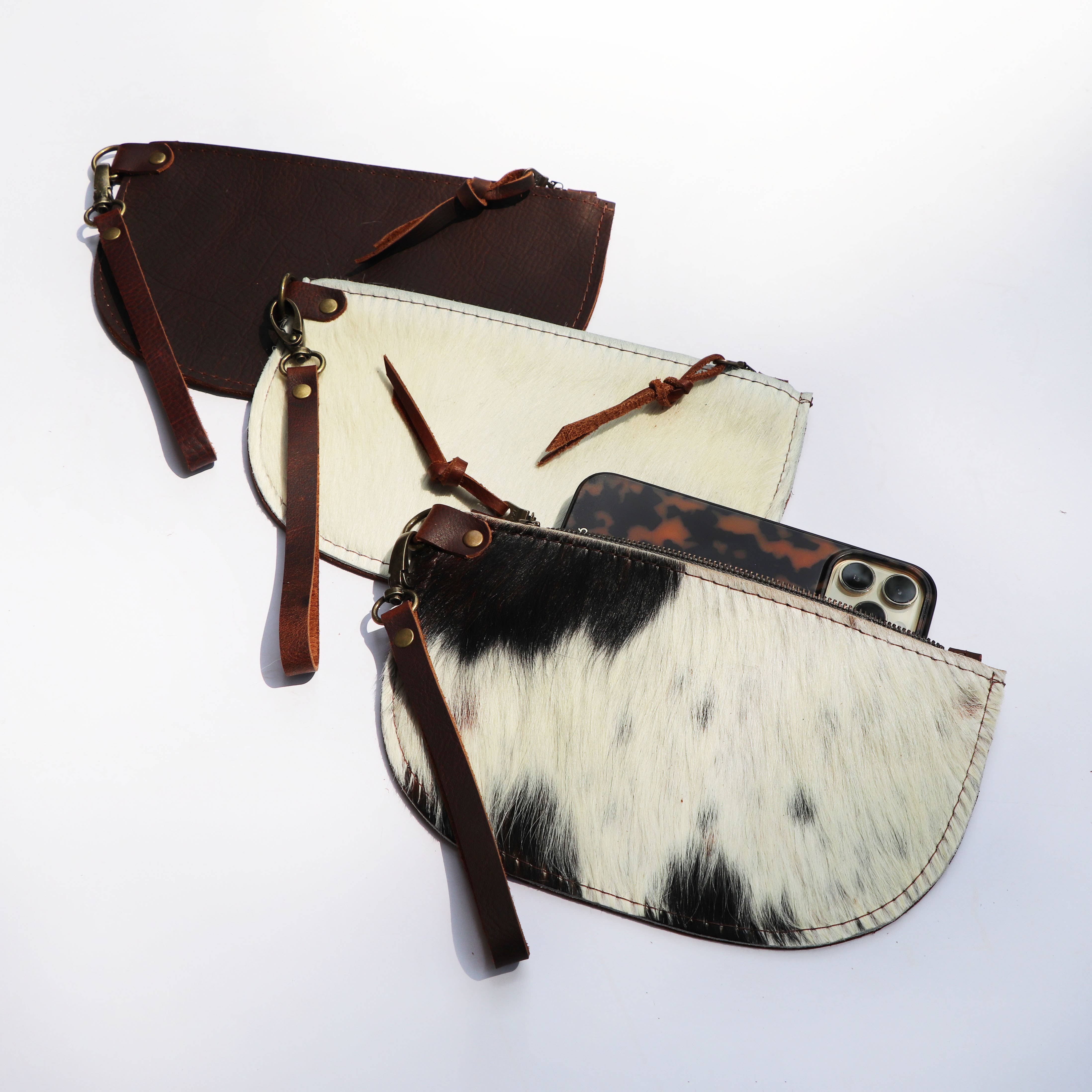 The Hawks & Doves Large Half Moon Cowhide and Leather Zip Pouch with Wristlet includes two patterned cowhide leather pouches and one large solid brown pouch, sized to hold a smartphone and a tortoiseshell-patterned item.