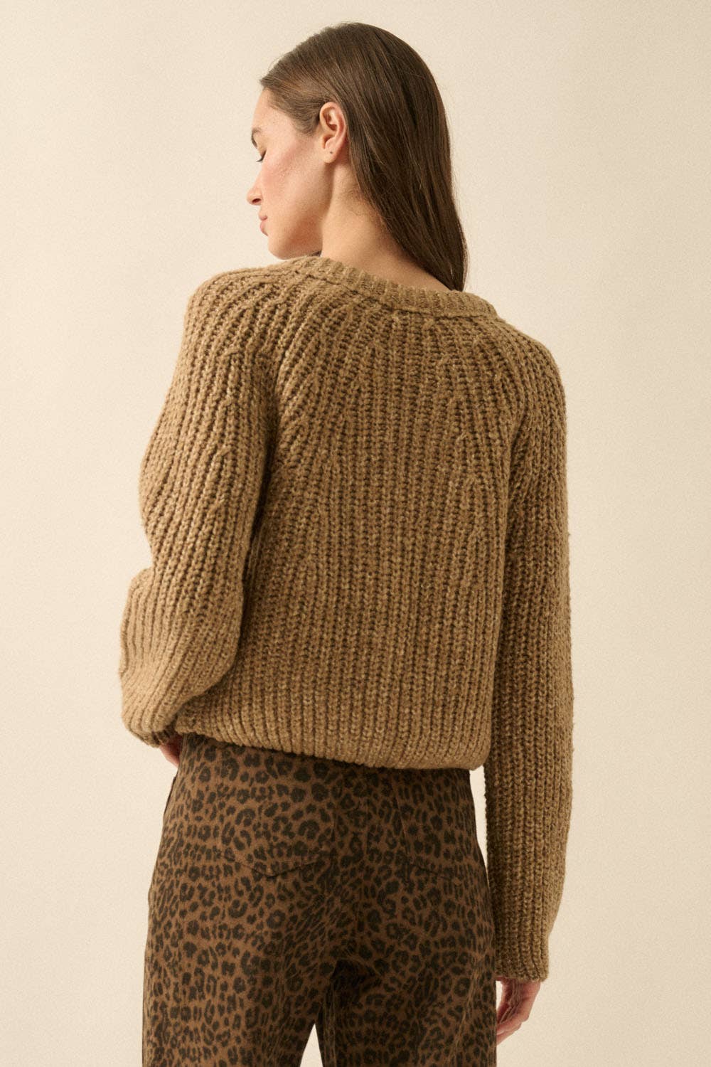 A woman with straight brown hair stands with her back to the camera, wearing Promesa USAs Confetti Button-Front Cardigan Sweater and high-waisted brown leopard print pants against a plain background.