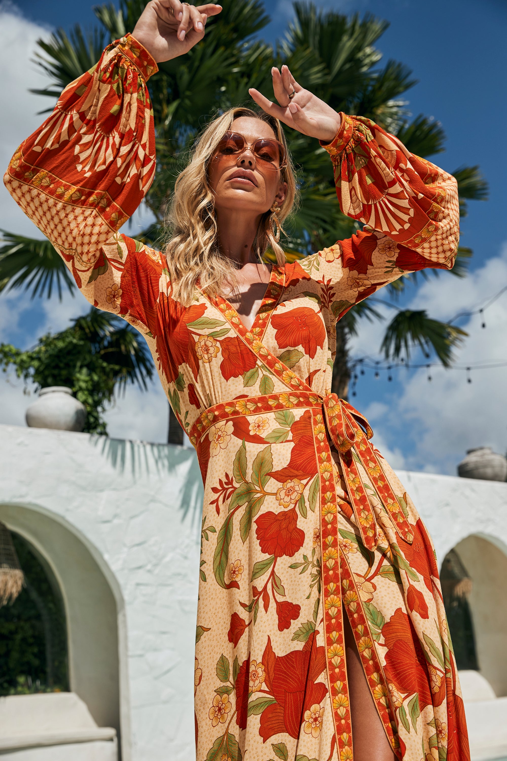 Woman in a floral dress posing outdoors with palm trees and a white building in the background