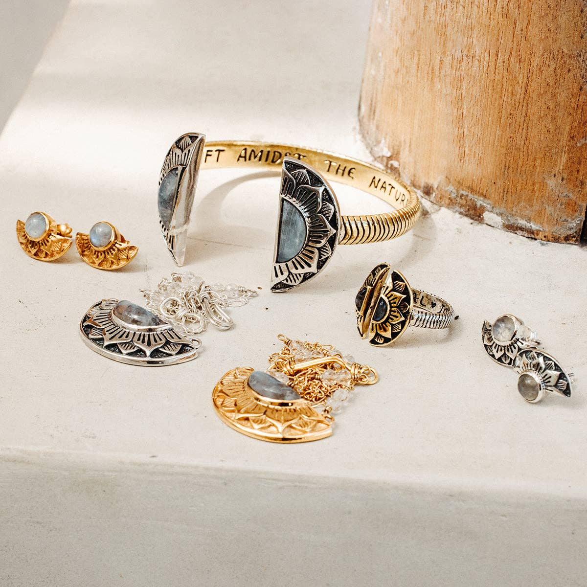 The bahgsu jewels Natural Mystic Ring - Moonstone is a two-toned, adjustable silver and gold ring with engraved designs and gemstone accents, displayed on a light surface near a wooden post.