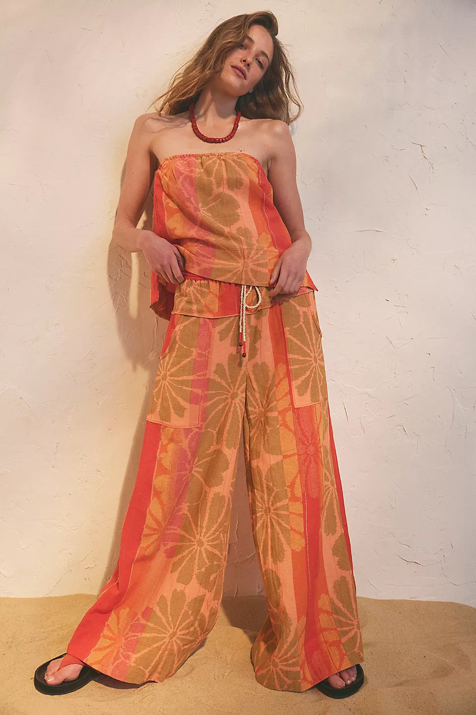 Woman wearing orange floral strapless top and wide leg pants set with a beaded necklace in FREE PEOPLE DEVELLA SET