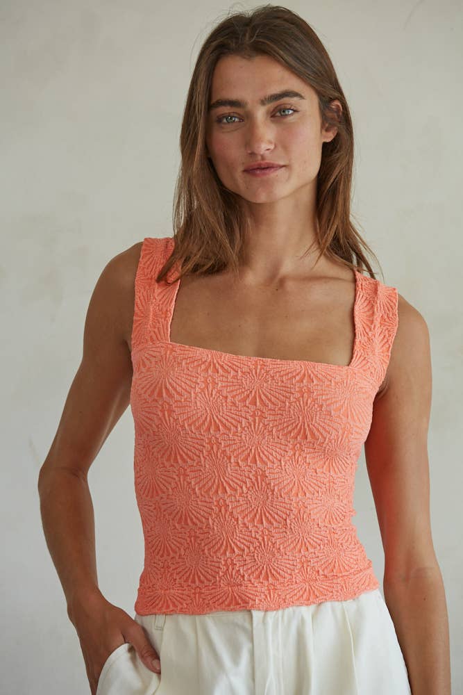 A woman with long brown hair wears the By Together Knit Modal Nylon Spandex Seamless Jacquard Tank in peach and white pants, standing against a light, neutral background while gazing at the camera with a relaxed expression.