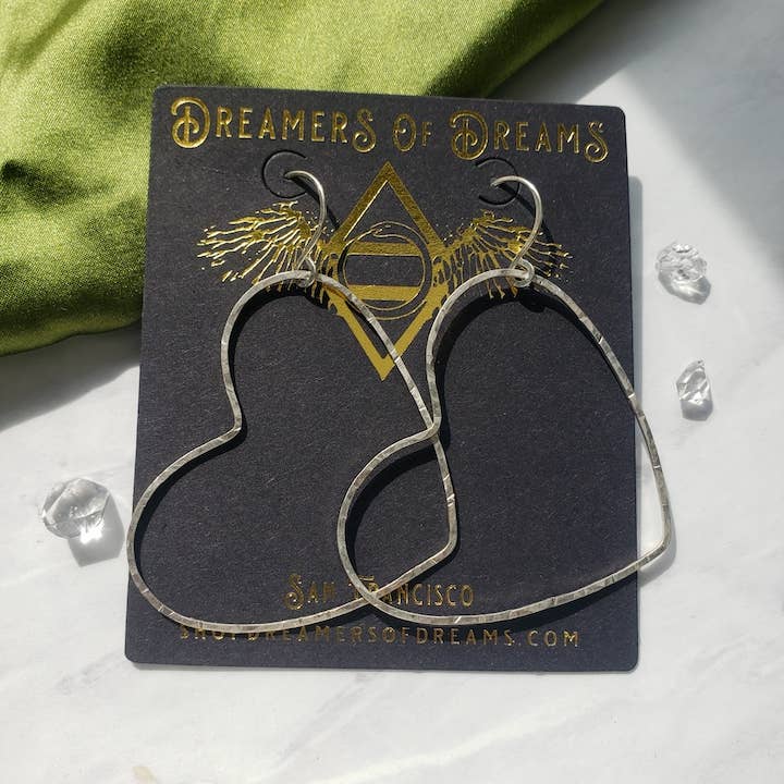 A Big Silver Heart - Paperclip Chain Necklace by Dreamers of Dreams is displayed on a black card, with green fabric and clear crystals in the background.