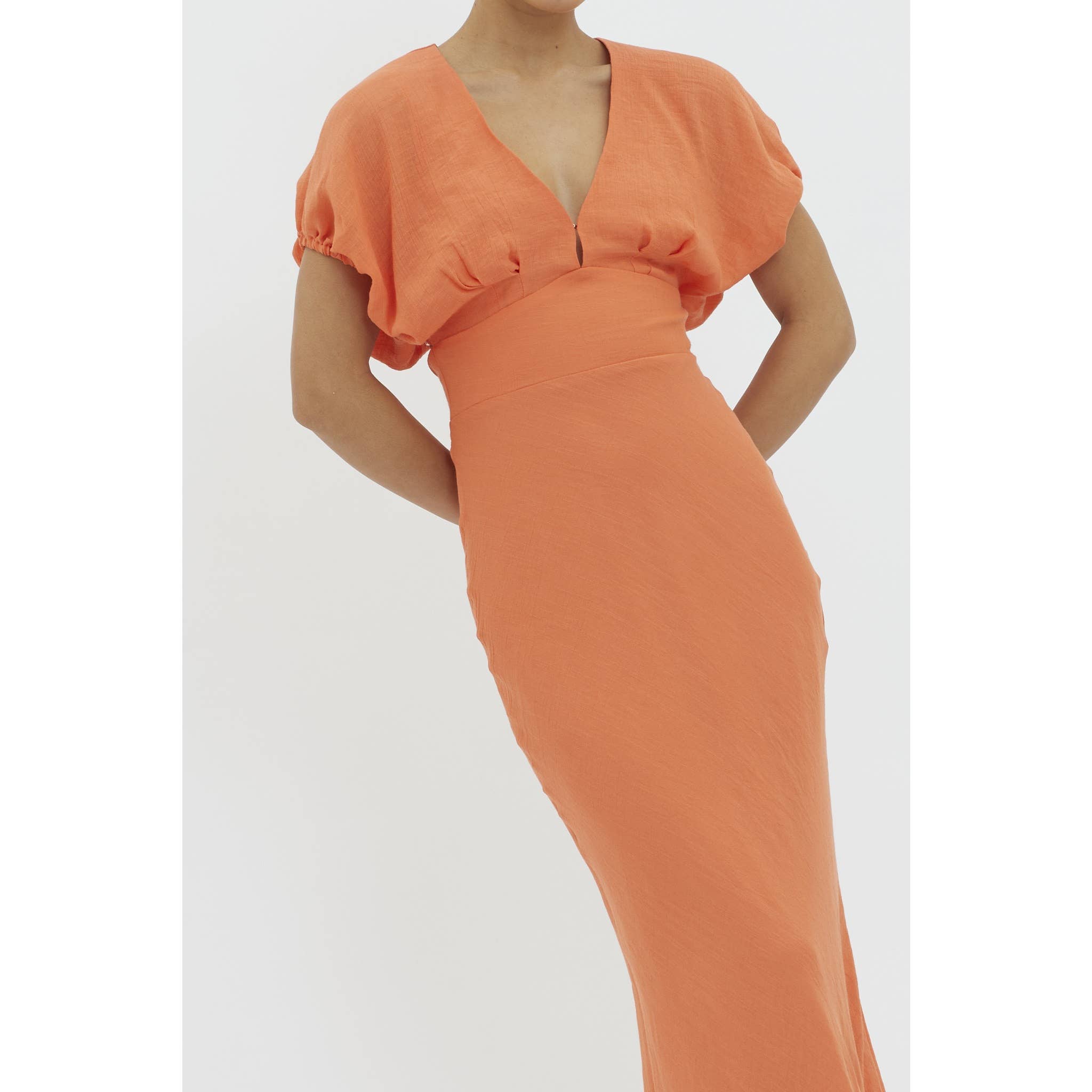 A person models the One and Only Collective Tangerine V-neck Maxi Dress with short puffy sleeves and an elastic waistband, standing against a plain white background. The photo is cropped at the shoulders and below the knees.