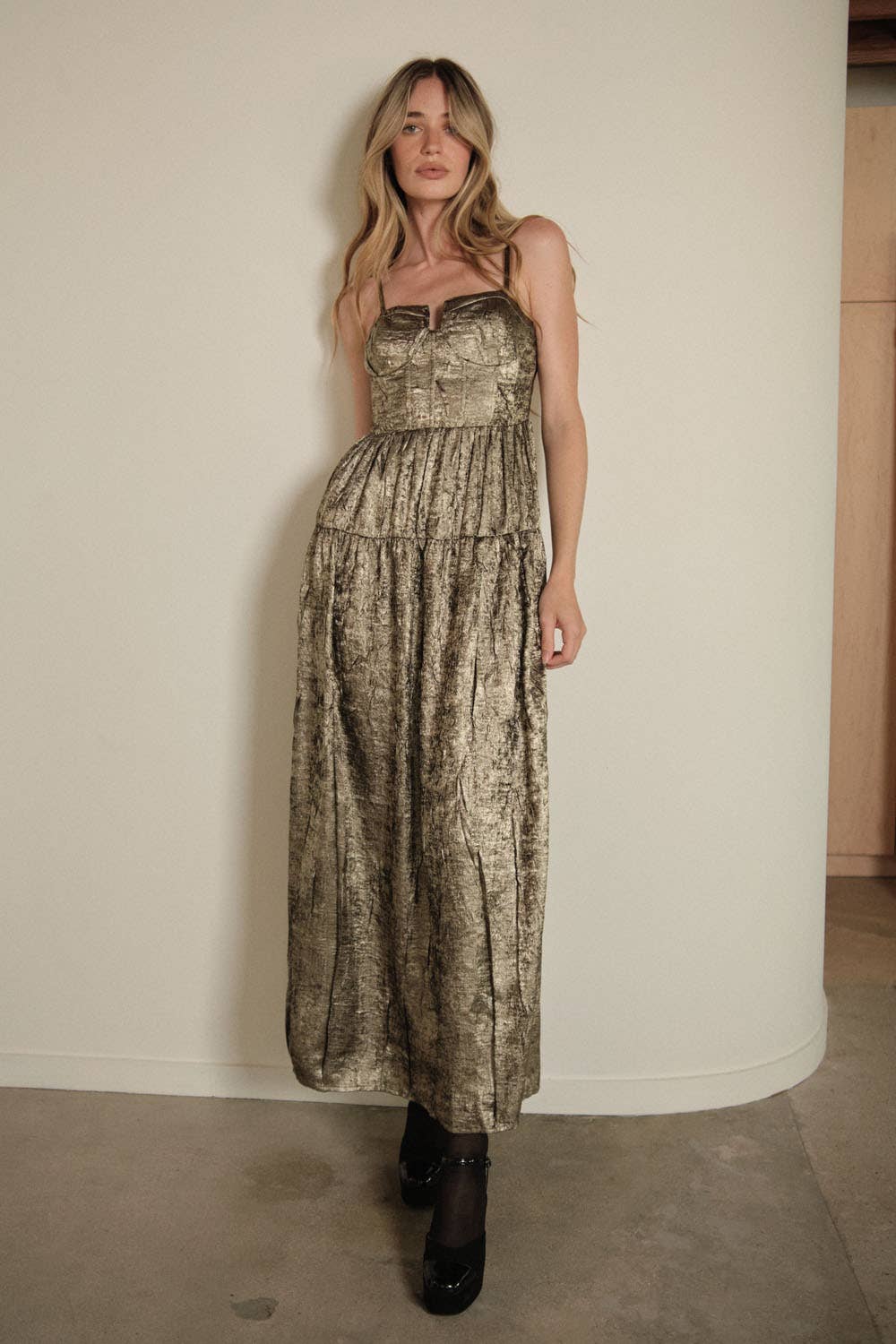 A woman with long blonde hair poses indoors against a plain light wall, wearing the Promesa USA Textured Metallic Fit-and-Flare Corset Maxi Dress and black platform shoes.