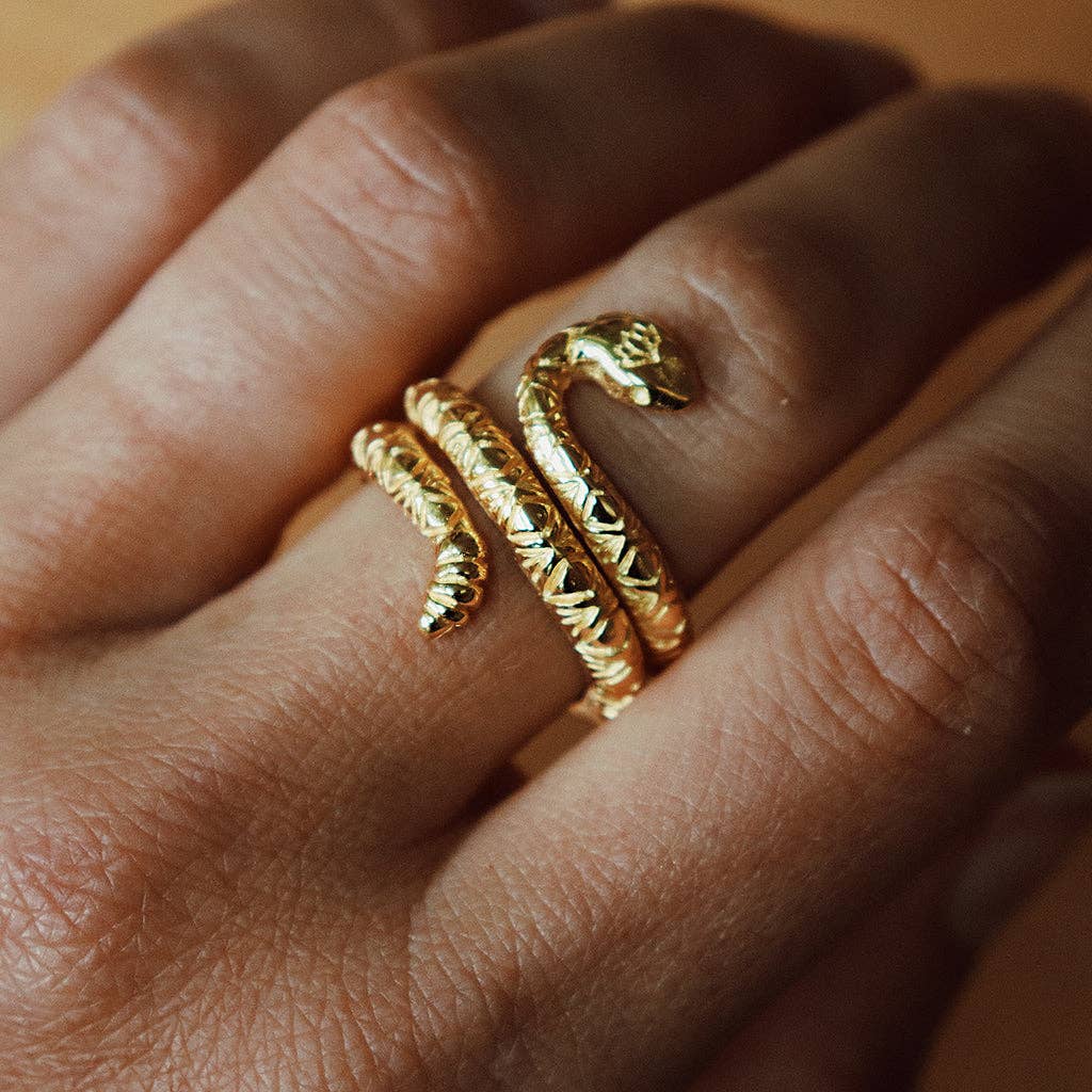 A close-up of a hand wearing the bahgsu jewels Rattlesnake Lotus Ring, a handcrafted brass piece shaped like a coiled serpent, featuring intricate scales and the visible snake’s head and tail on the finger.