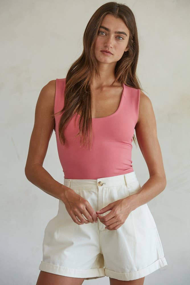 Woman wearing a sleeveless pink Double Layered Seamless Top paired with high-waisted white shorts in soft light.