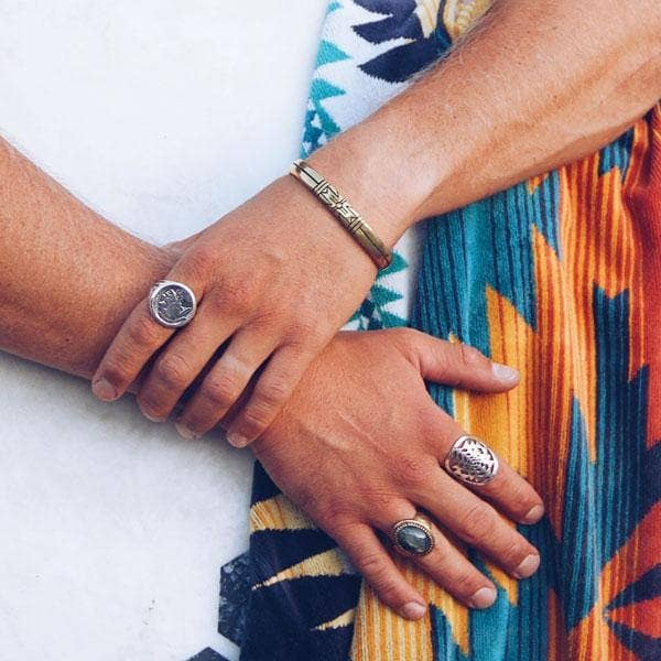 Close-up of hands wearing the Medicine Wheel Cuff || Men and multiple bold silver rings on colorful fabric background