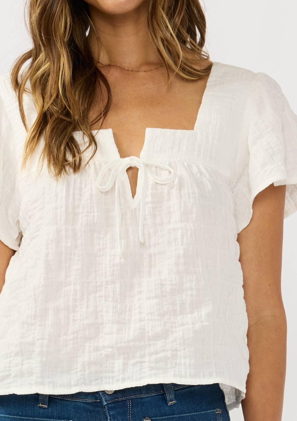 Woman wearing a white Square Neck Puff Sleeve Gauze Top with delicate tie-front detail and textured fabric