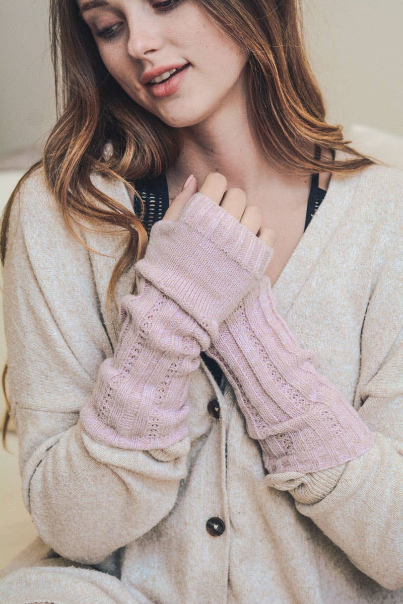 A young woman with long hair wears Leto Accessories Ribbed Arm Warmers in pale pink and a cream cardigan, sitting indoors with a soft smile.