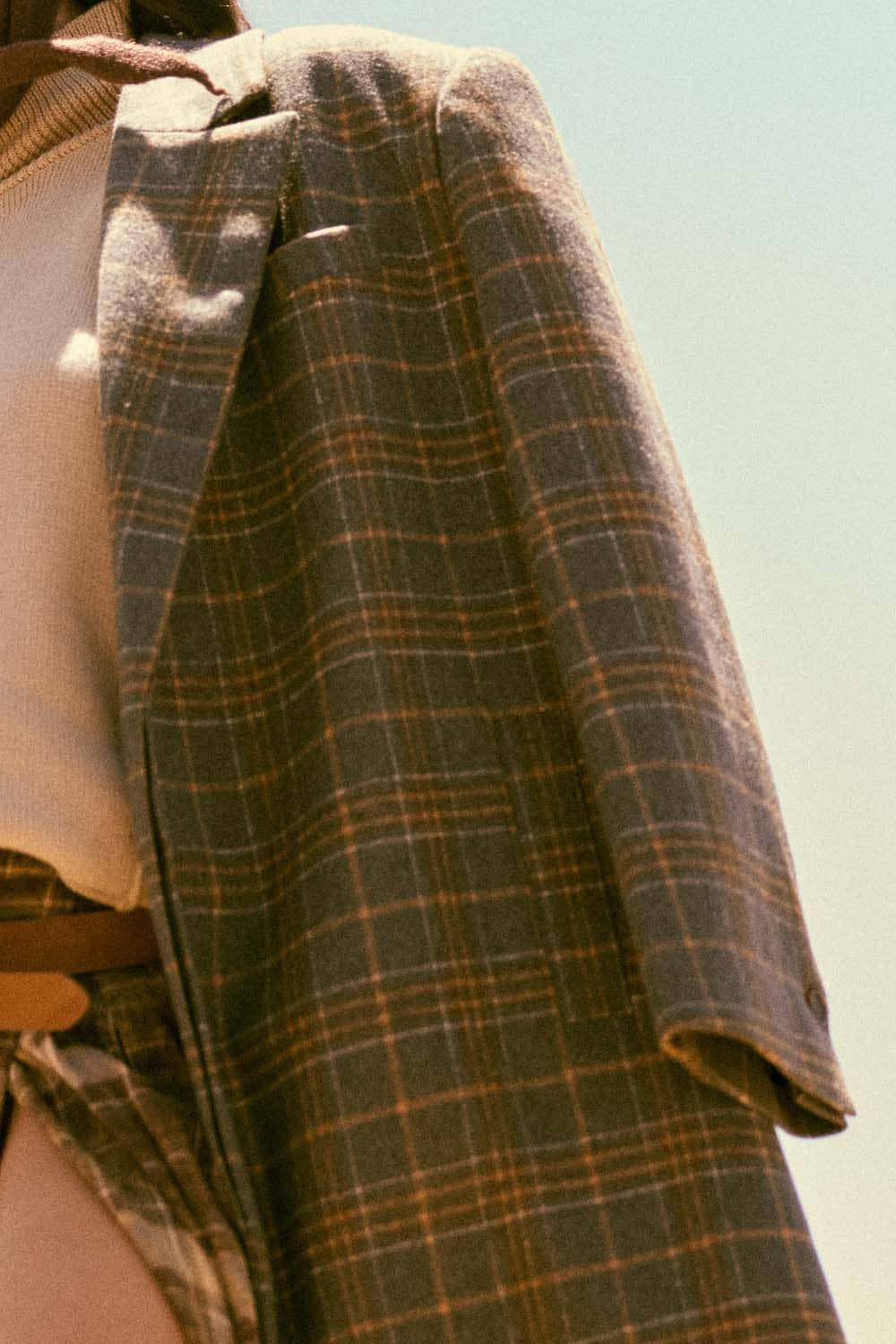 A person wears the Plaid Felt Double-Breasted Calf-Length Overcoat by Promesa USA over a beige sweater, standing outside from shoulders to waist, with soft sunlight creating a warm atmosphere.