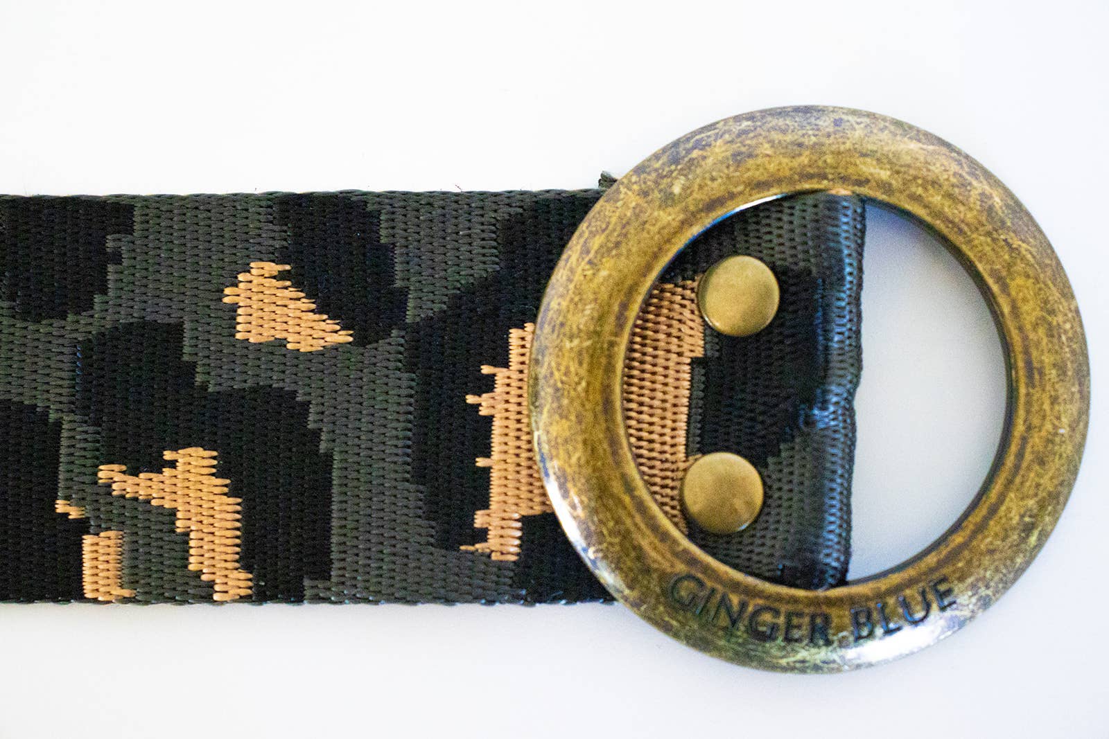 A close-up of the Ginger Blue Wild Child Leopard belt shows its black and tan leopard print, round worn brass buckle stamped GINGER BLUE, and two metal studs securing the belt end for a bold cinch style.