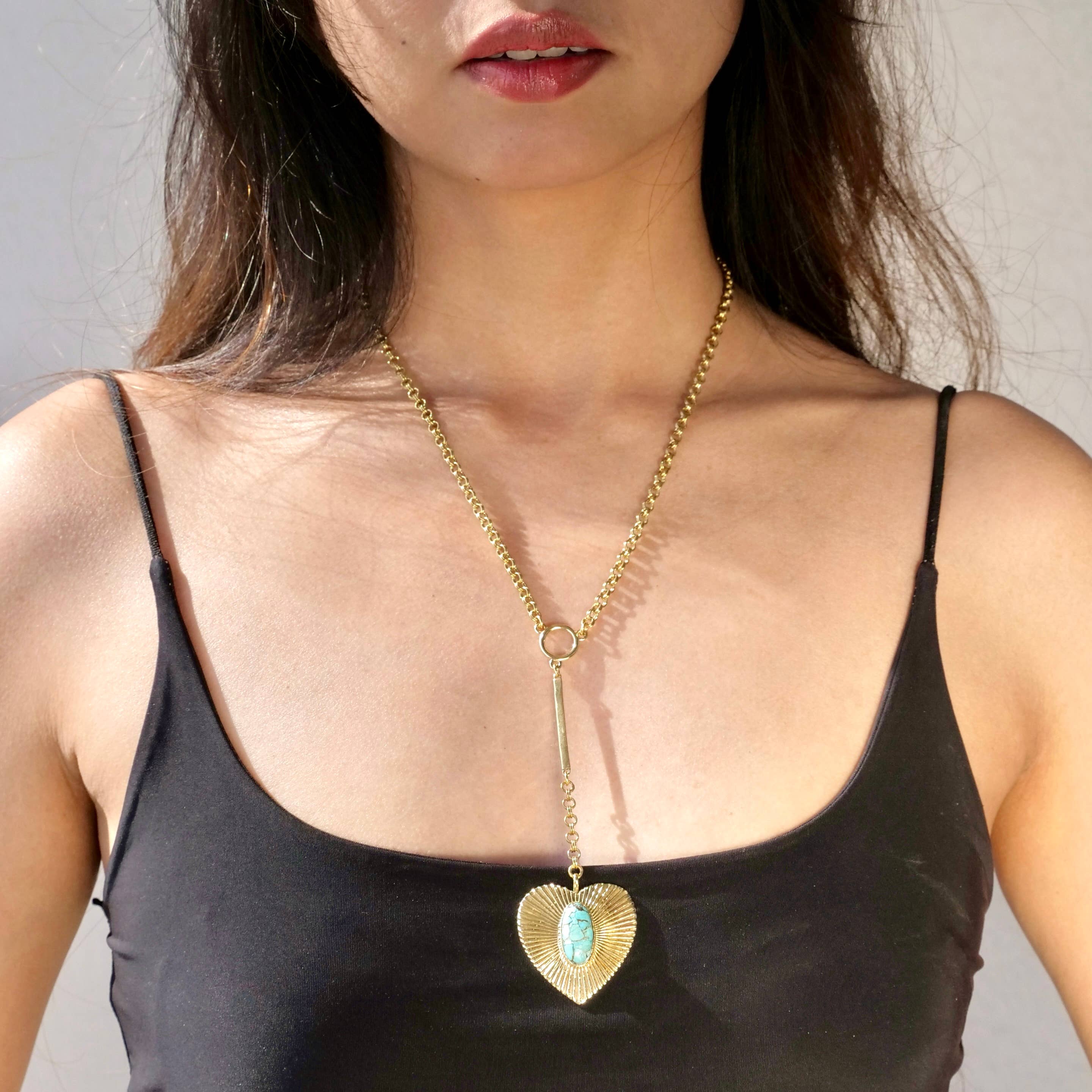 Brass Turquoise Heart Necklace worn on a woman with a black tank top showcasing the pendant’s turquoise center stone and chain