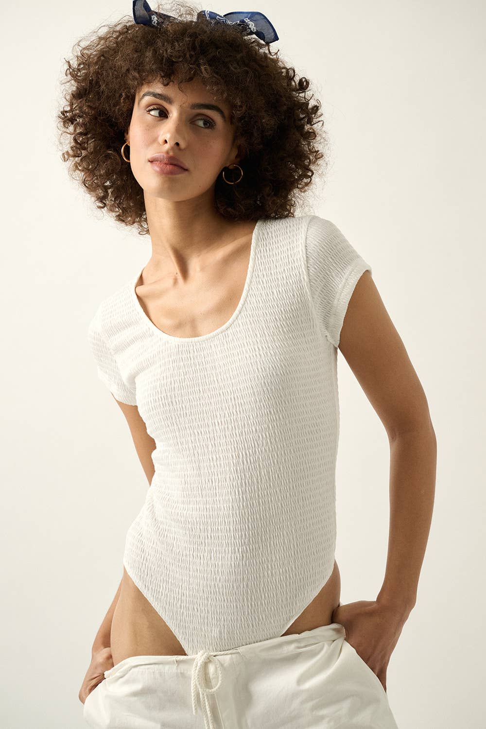 Woman wearing a white Smocked Jersey Scoop Neck Bodysuit with short sleeves and textured fabric, styled casually