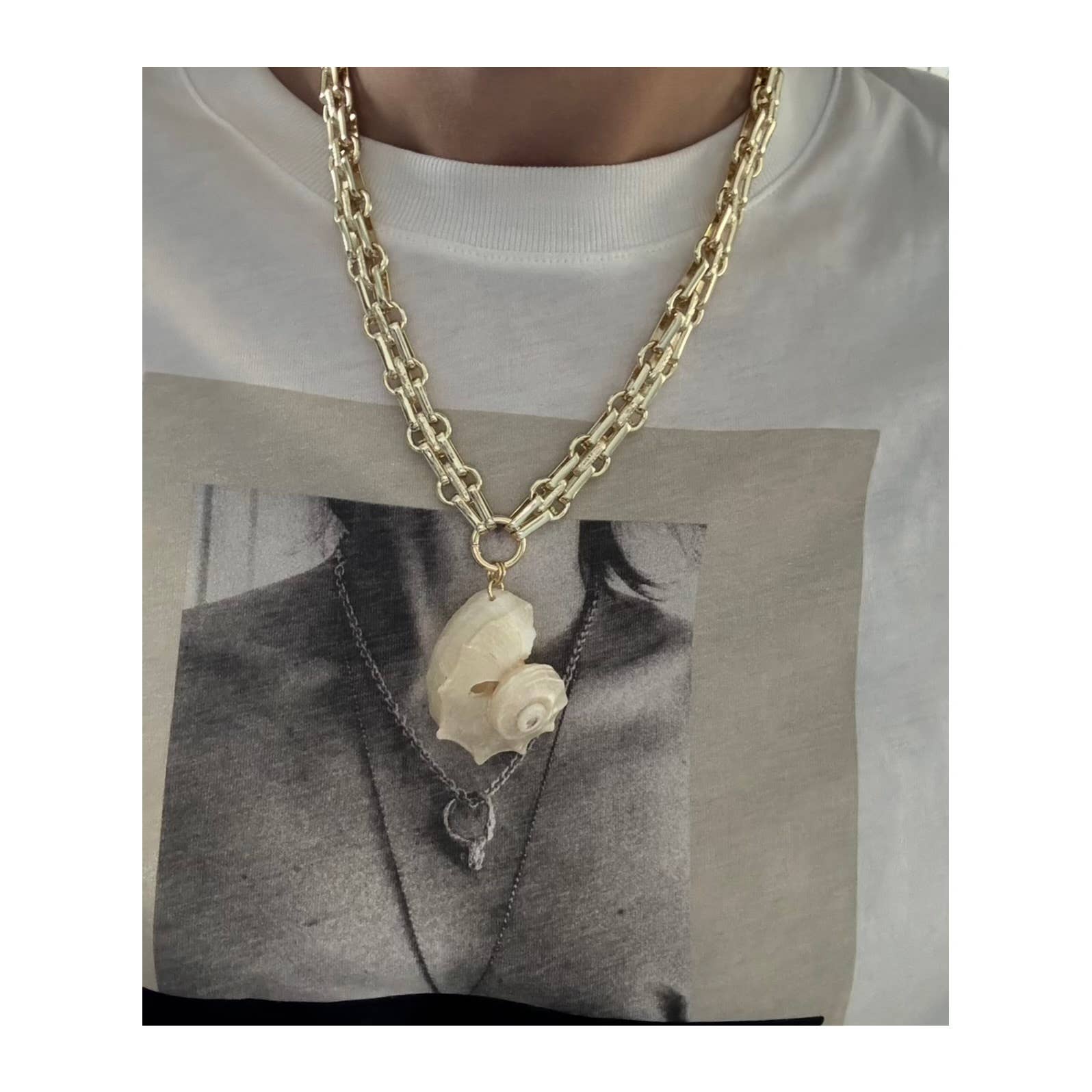 A person wears the Tramps+Thieves Golden Nautilus Necklace—a gold-filled chain with a striking white seashell pendant—layered over a white tee that displays a black and white print of another necklace with a pendant.