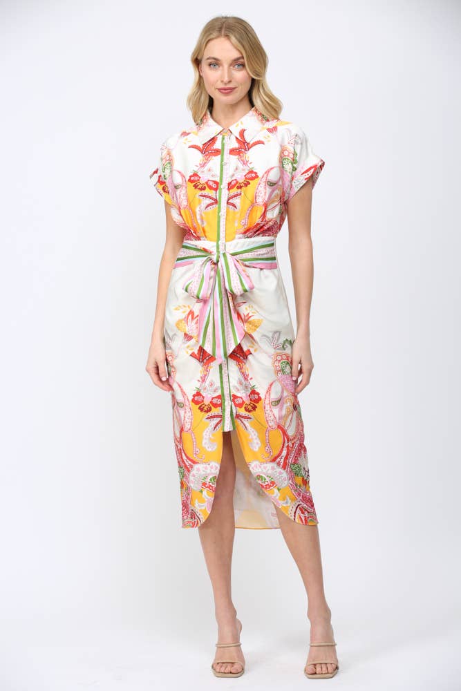 Woman wearing BOTANIC SCARF PRINT SELF TIE WAIST BUTTON DOWN DRESS with vibrant colors and floral pattern standing against white background