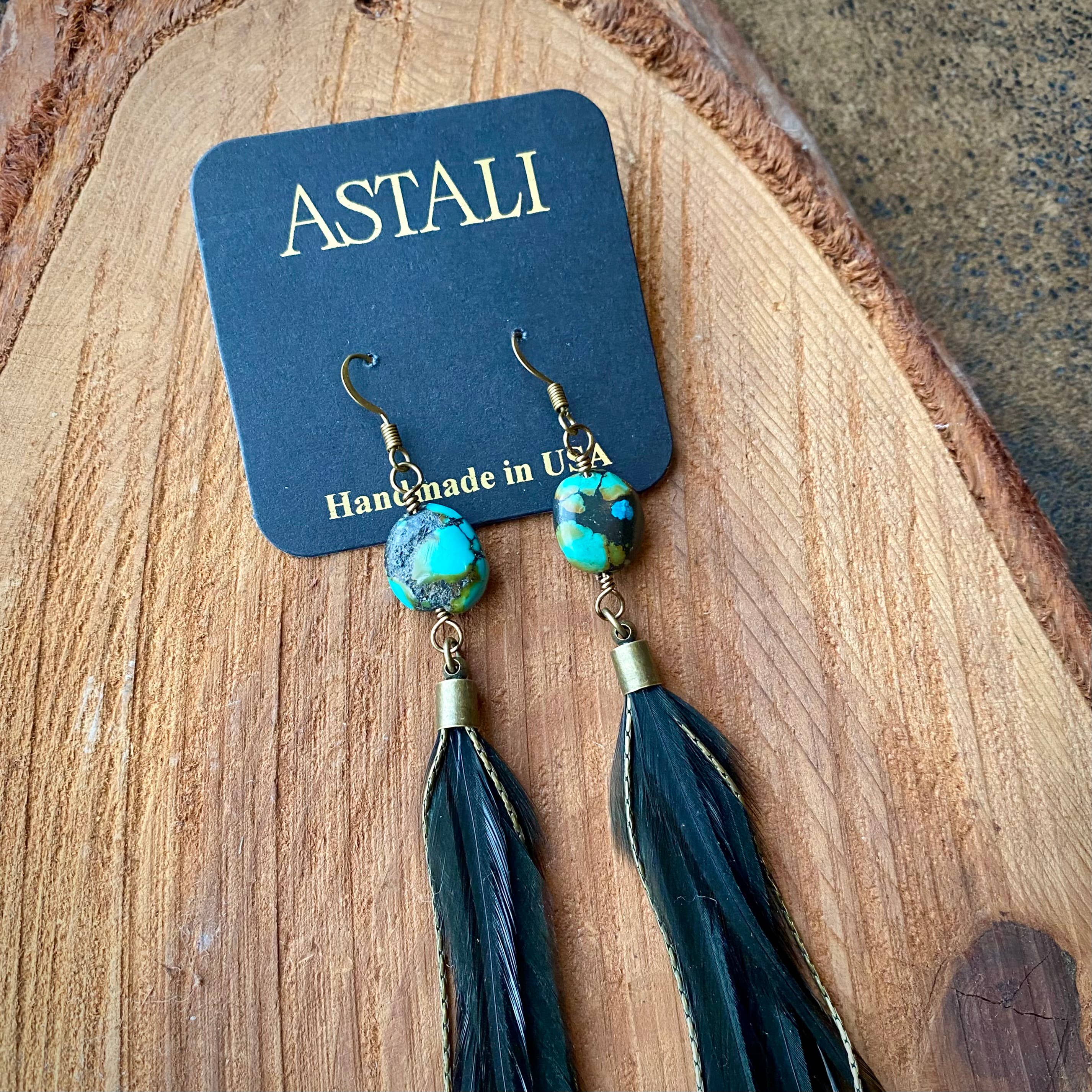 ASTALI’s Feather & Turquoise Statement Earrings feature antique brass, turquoise beads, and sustainably sourced black coque feathers, displayed on a branded card—perfect for eco-conscious jewelry lovers.