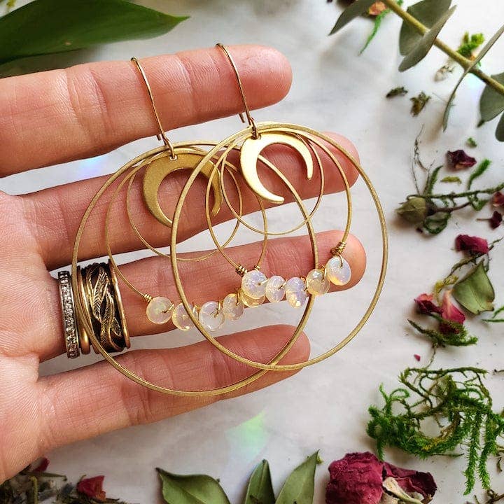 Opal Moon Halo Hoop Earrings with gold crescent moons and opal beads on thin gold hoops held by a hand over dried flowers