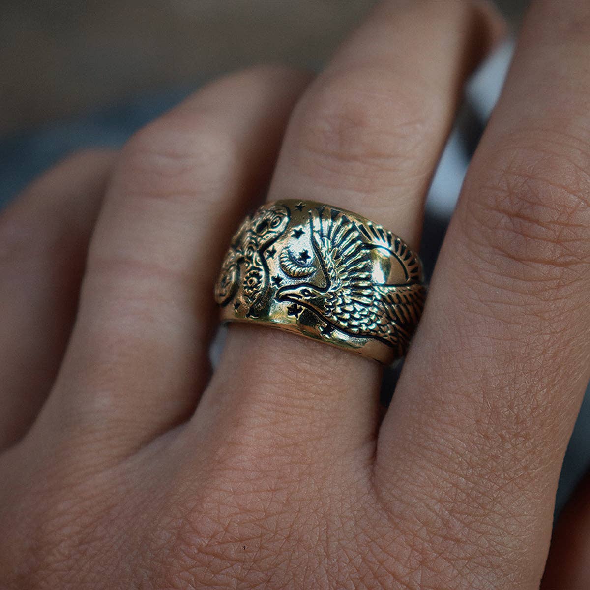 A close-up of a hand wearing the Rainbow Serpent Ring from bahgsu jewels Xavier Rudd Collaboration, showcasing a wide gold statement design engraved with detailed serpent patterns.