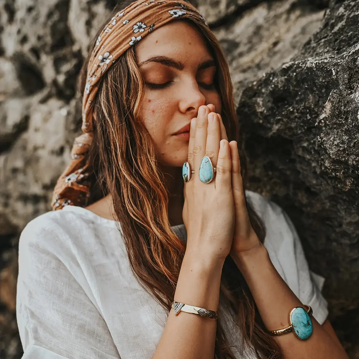 Woman wearing turquoise gemstone rings and a Hold Space Cuff, posing peacefully with eyes closed near a rocky wall