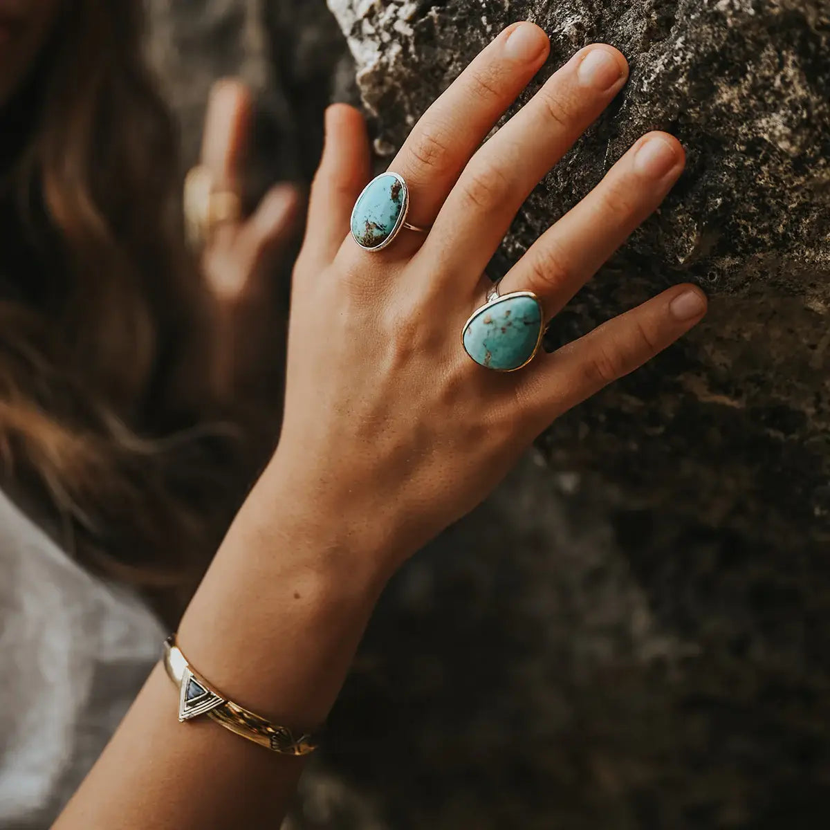 Hand wearing turquoise rings and gold bracelet with Hold Space Cuff resting on textured stone surface