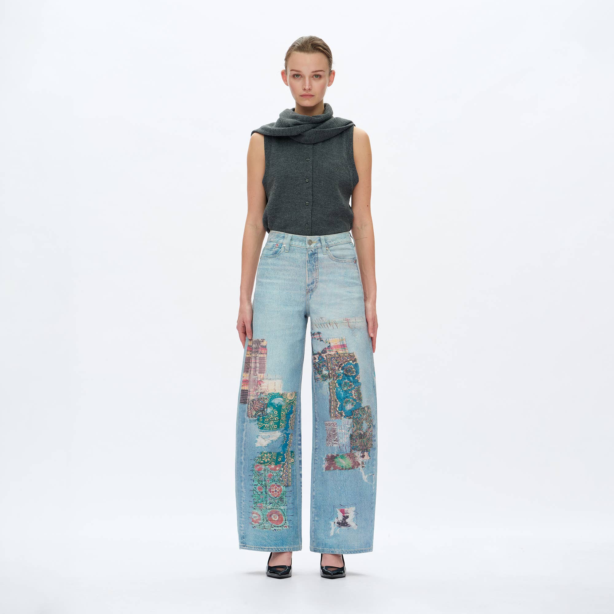 A woman poses against a white background in BAYEAS Light Blue Patch Pattern High-Rise Barrel Jeans paired with a sleeveless gray top featuring a scarf collar and black pointed-toe heels.
