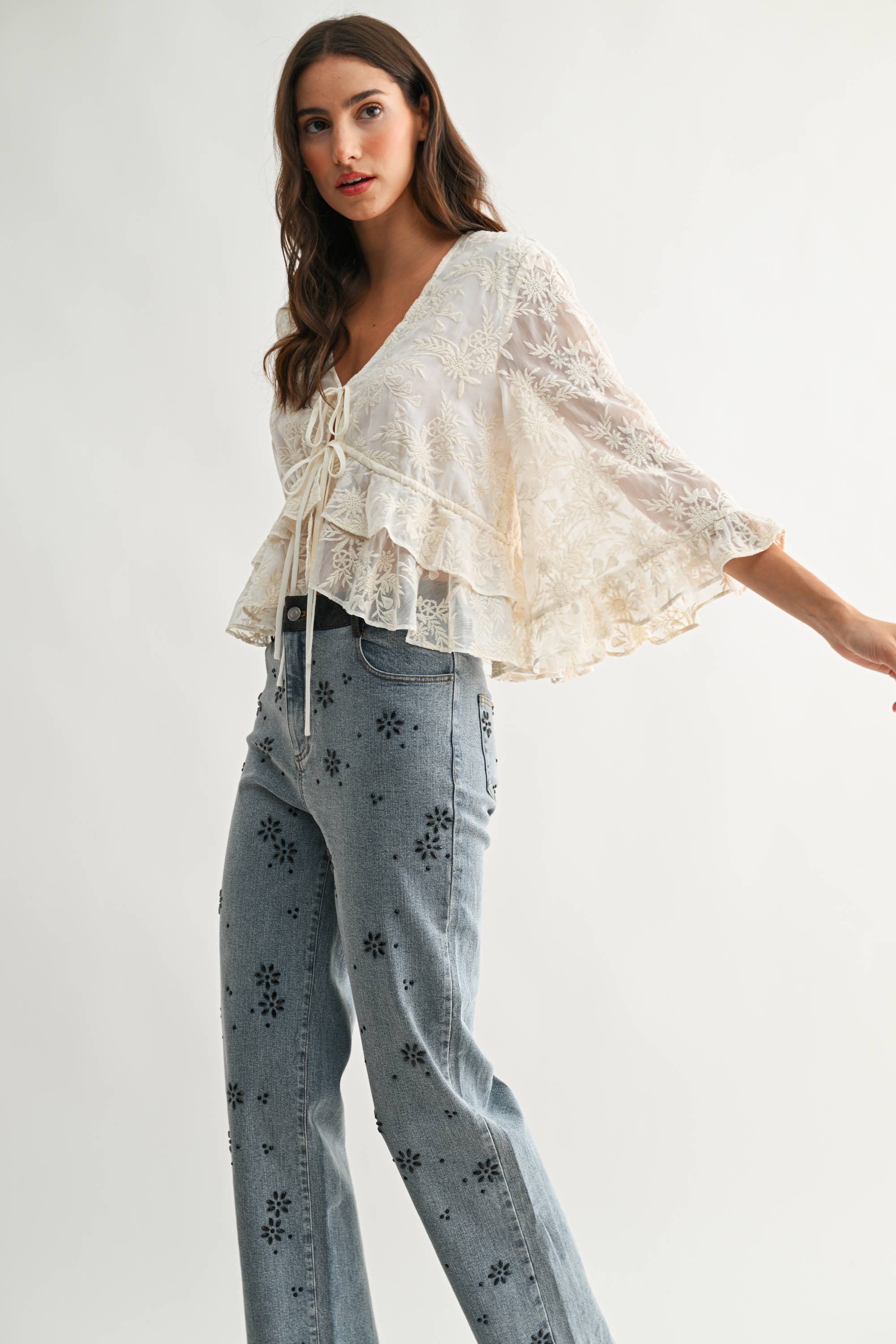 Woman wearing Boho Embroidered Sheer Blouse with flowing sleeves paired with patterned denim jeans in soft lighting