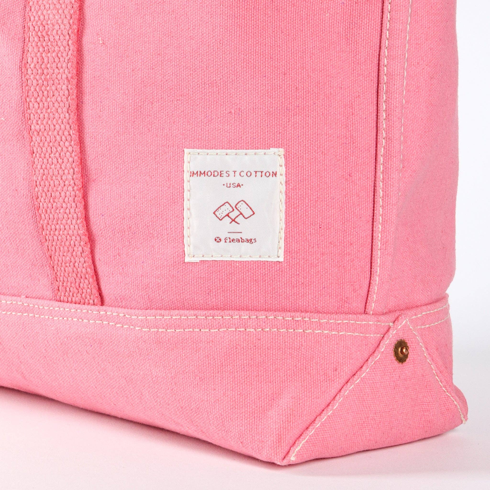 Close-up of pink canvas bag corner with white stitched label and durable base detail Small East West Tote | Flamingo
