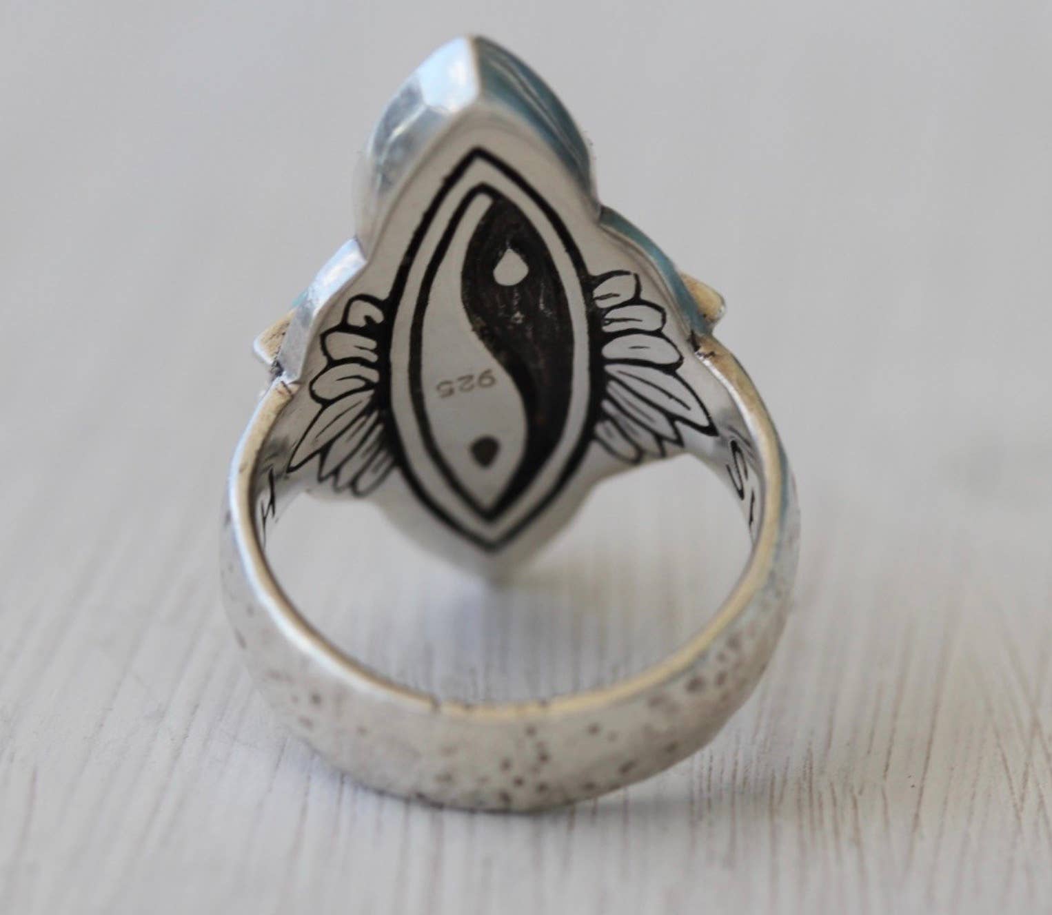 The bahgsu jewels Truth Seeker Ring is a sterling silver piece with yin-yang and feather engravings, marked 925 on the inner band. This unique ring is displayed on a light wooden surface.
