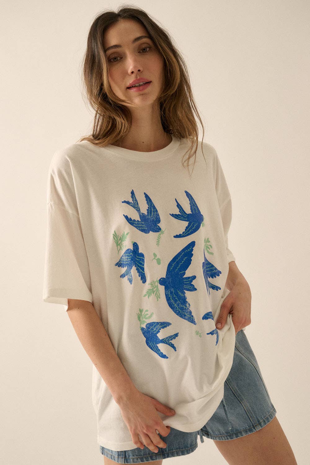 Woman wearing a Vintage Birds Garment Washed Oversized Graphic Tee with blue birds and green leaves paired with denim shorts
