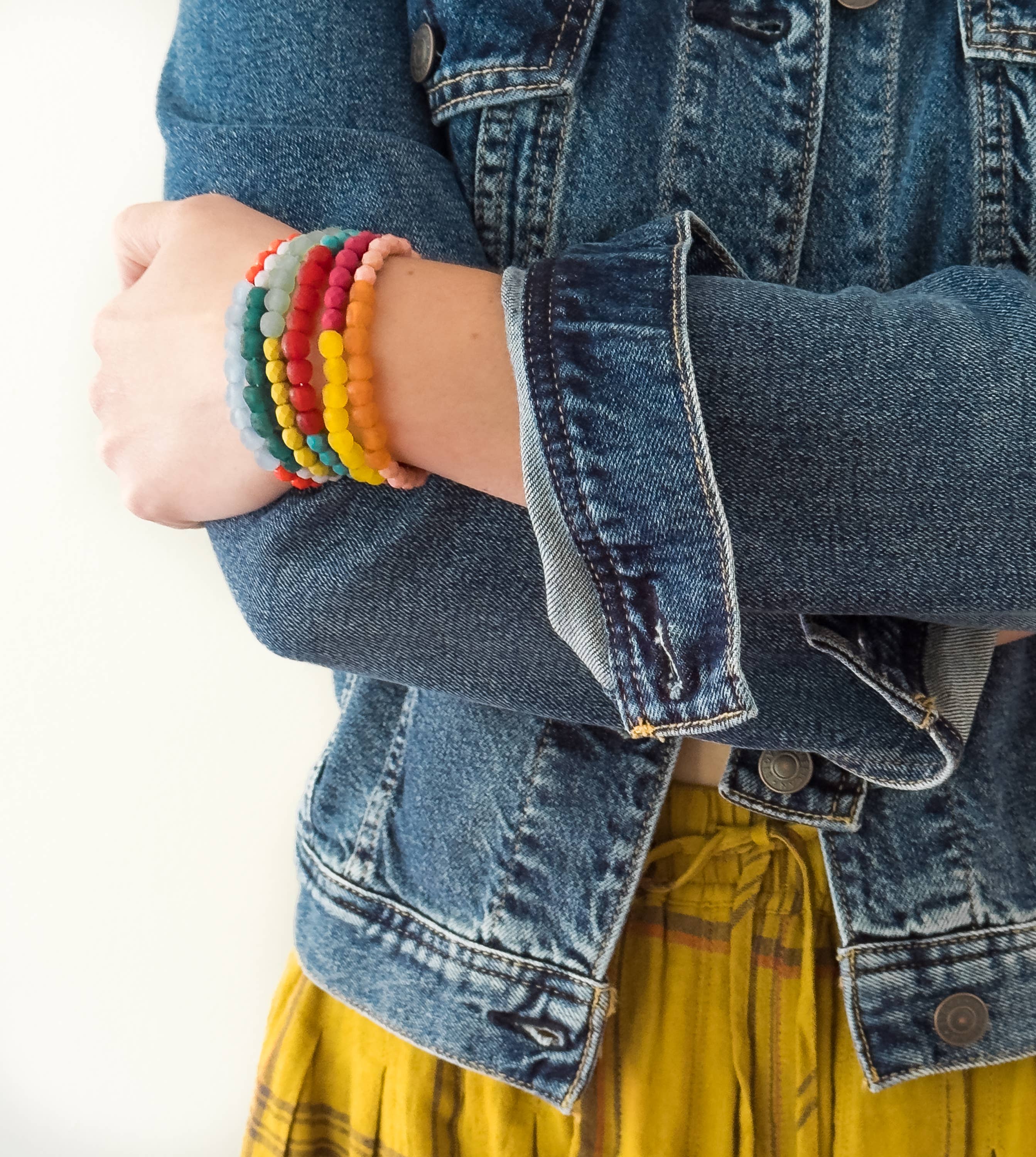 Person wearing a denim jacket and yellow skirt with colorful Multicolor Recycled African Glass And Mixed Bead Bracelet stacked on wrist