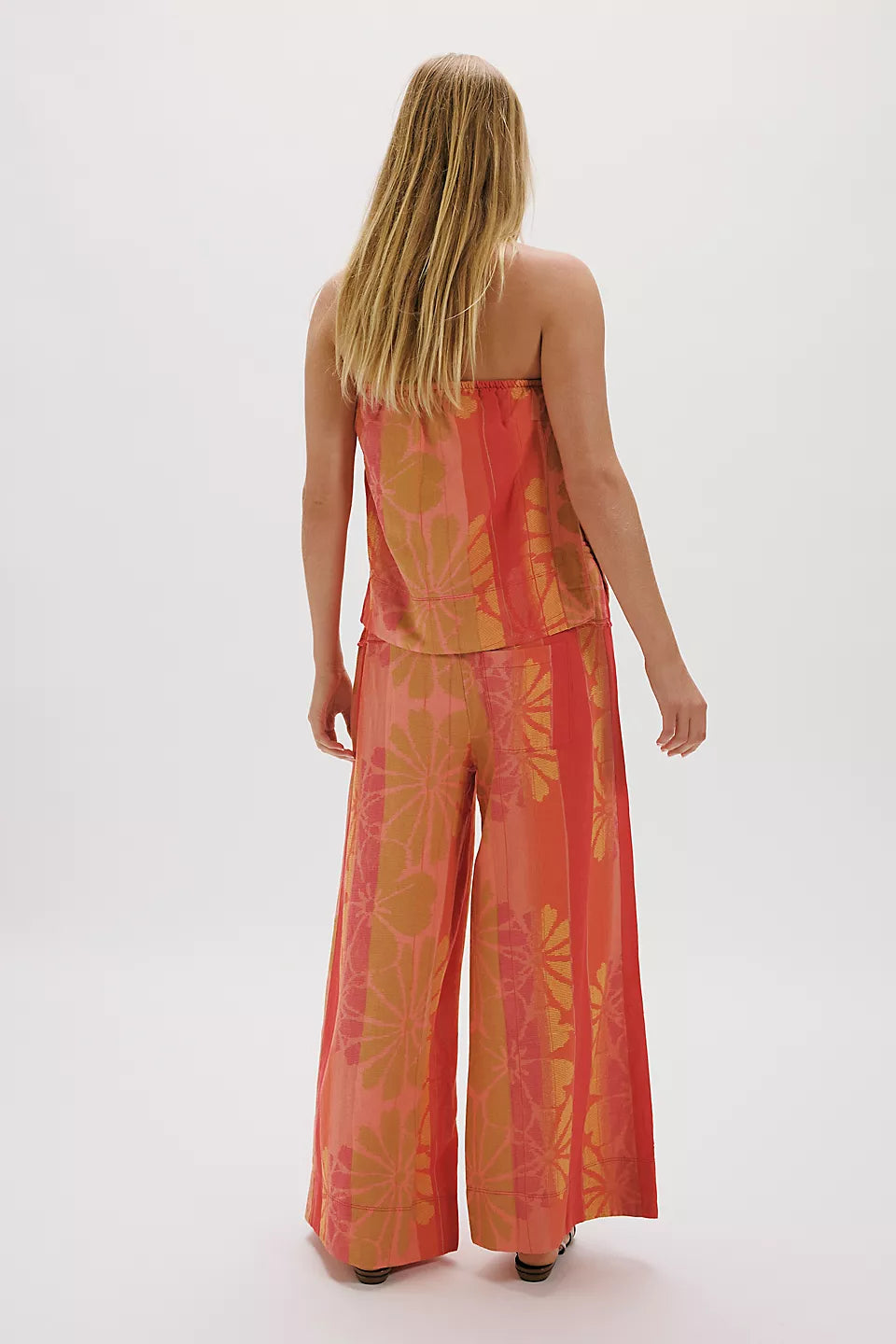 Woman wearing FREE PEOPLE DEVELLA SET with orange floral wide-leg pants and strapless top, standing against white background.