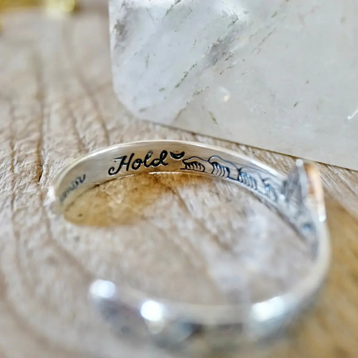 Close-up of a silver Hold Space Cuff with delicate engraved wave designs on a wooden surface.