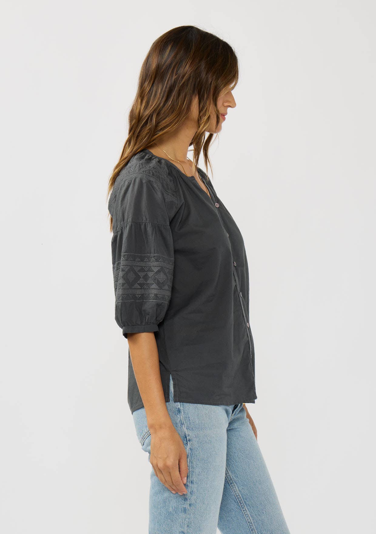 Woman wearing a black Short Raglan Puff Sleeve Button Down Top with embroidered sleeves and light blue jeans side view