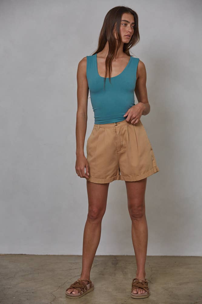 A woman with long brown hair stands against a plain background in a By Together Double Layered Seamless Top in teal, paired with tan high-waisted shorts and tan sandals. She looks slightly to the side with a relaxed posture.