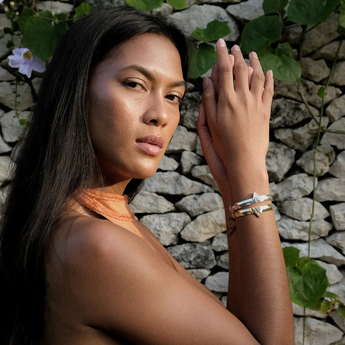 Woman wearing a Hold Space Cuff bracelet, posing outdoors with stone wall and greenery background