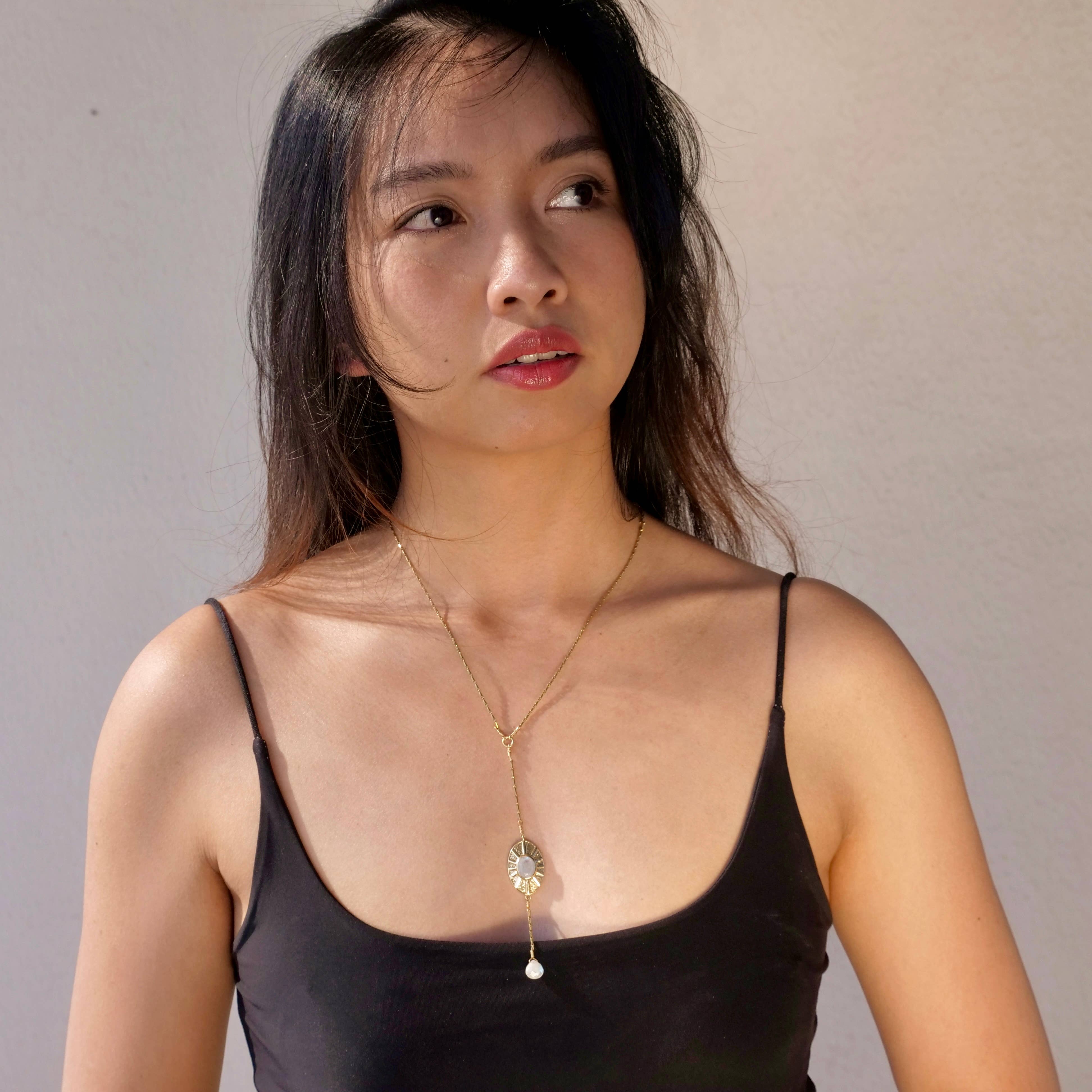 Woman wearing a delicate Sun Goddess Moonstone Necklace with gold chain and pearl drop pendant styled with black tank top