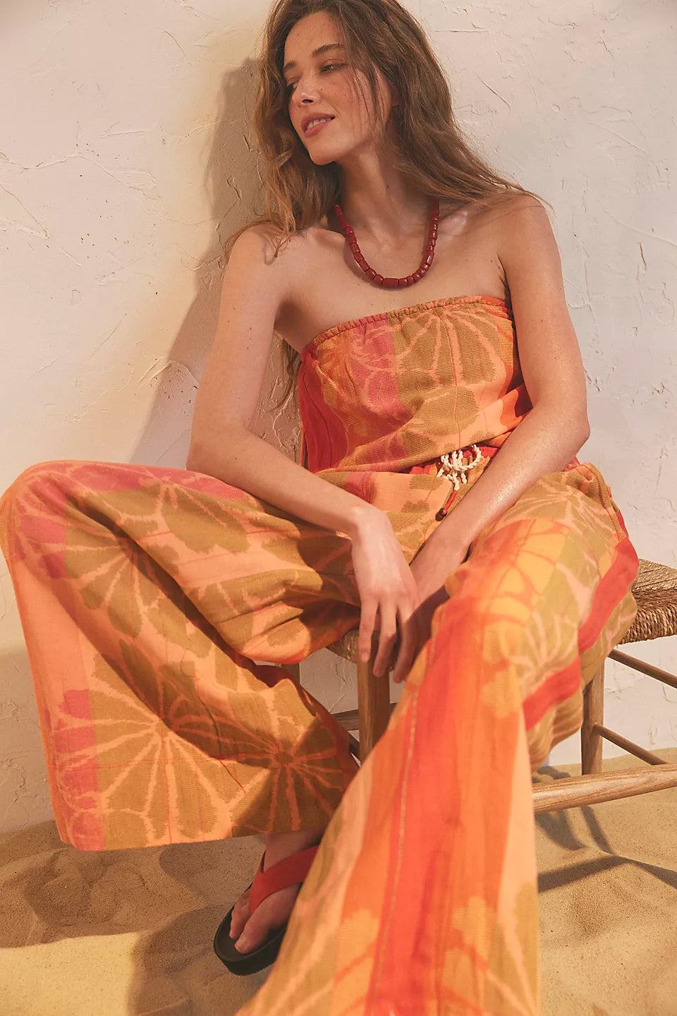 Woman seated wearing FREE PEOPLE DEVELLA SET with warm orange and brown floral patterns and wide-leg pants.
