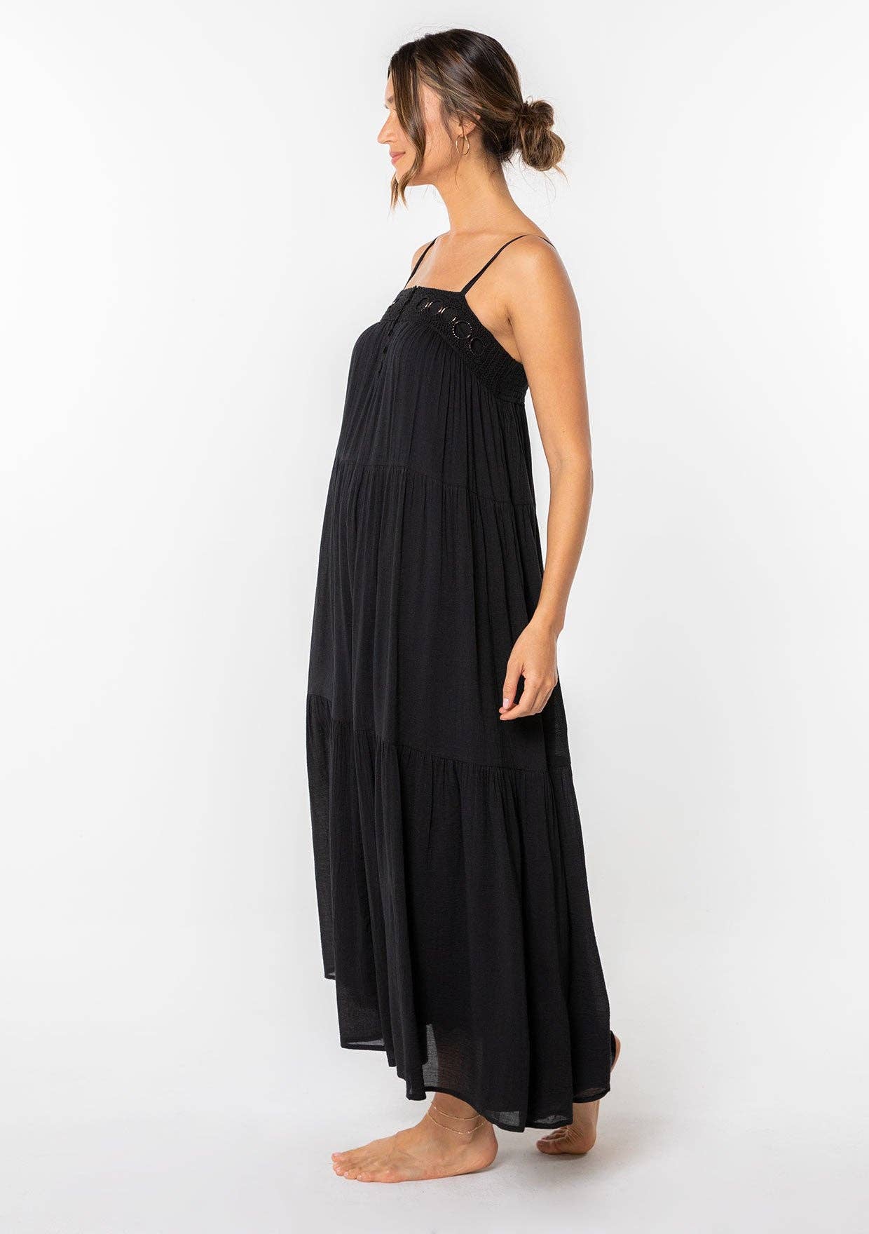 Woman standing barefoot wearing a black Bohemian Crochet Tiered Maxi Dress with spaghetti straps and crochet details